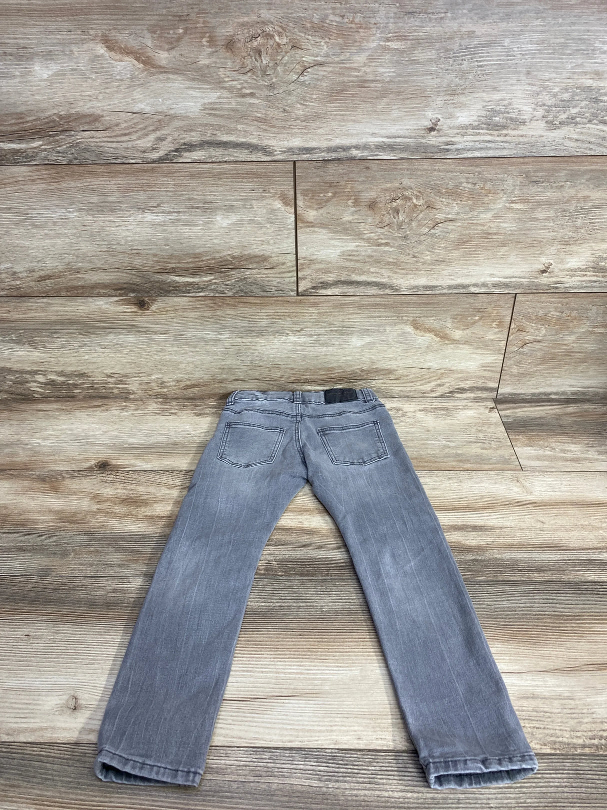Back view of gray children's jeans with pockets on wood floor background