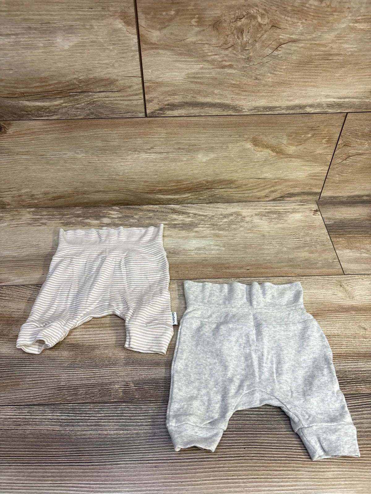 Top view of Gerber newborn pants, one solid gray pair and one gray striped pair on a wood-look floor