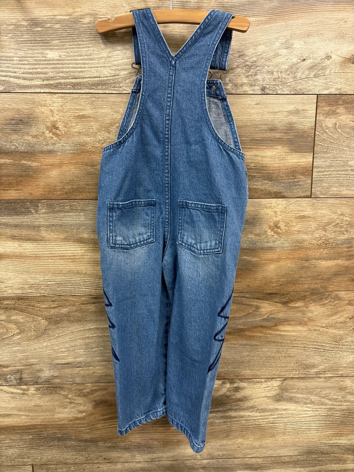 Front view of Juno Valentine toddler overalls showcasing front pockets and embroidered lightning bolts on a wooden backdrop
