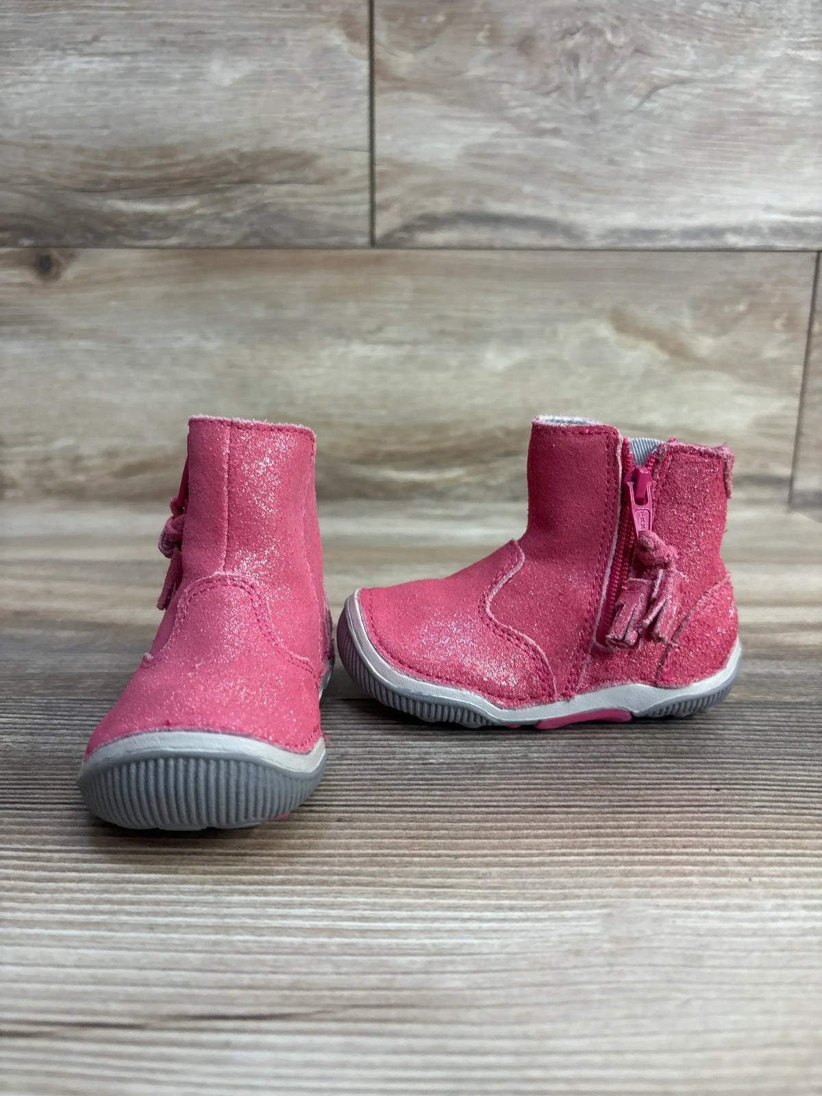 Pair of pink toddler boots with glittery finish and gray soles on wooden surface
