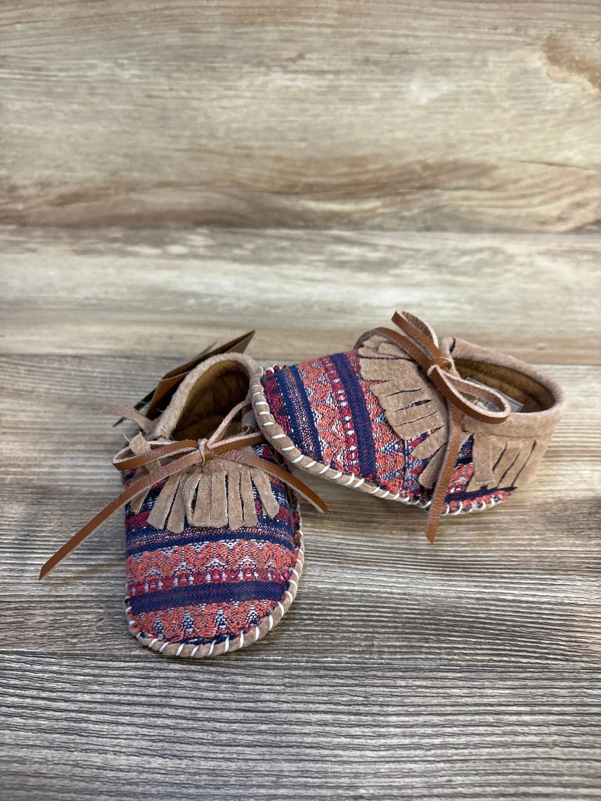 Patterned baby moccasins with suede fringe and laces on wooden background