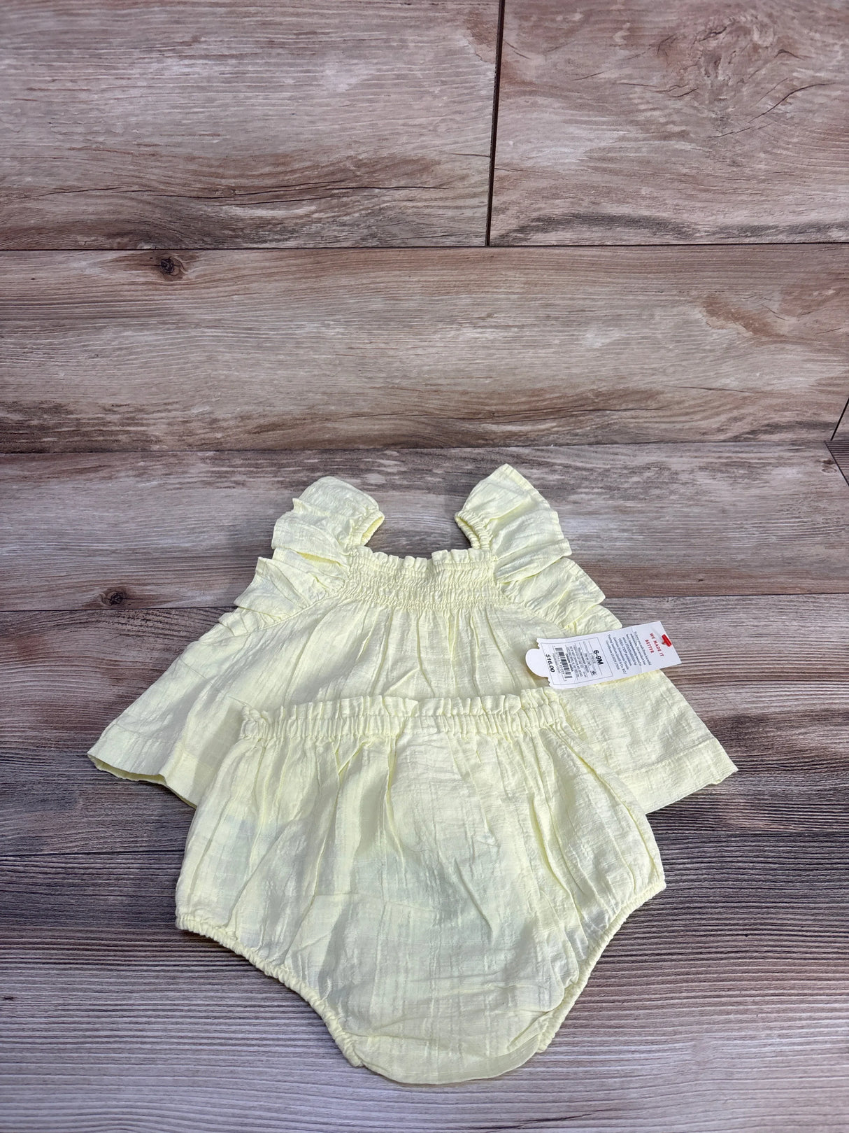 Top-down view of yellow two-piece baby set with ruffled sleeveless top and elastic bloomers on wood background