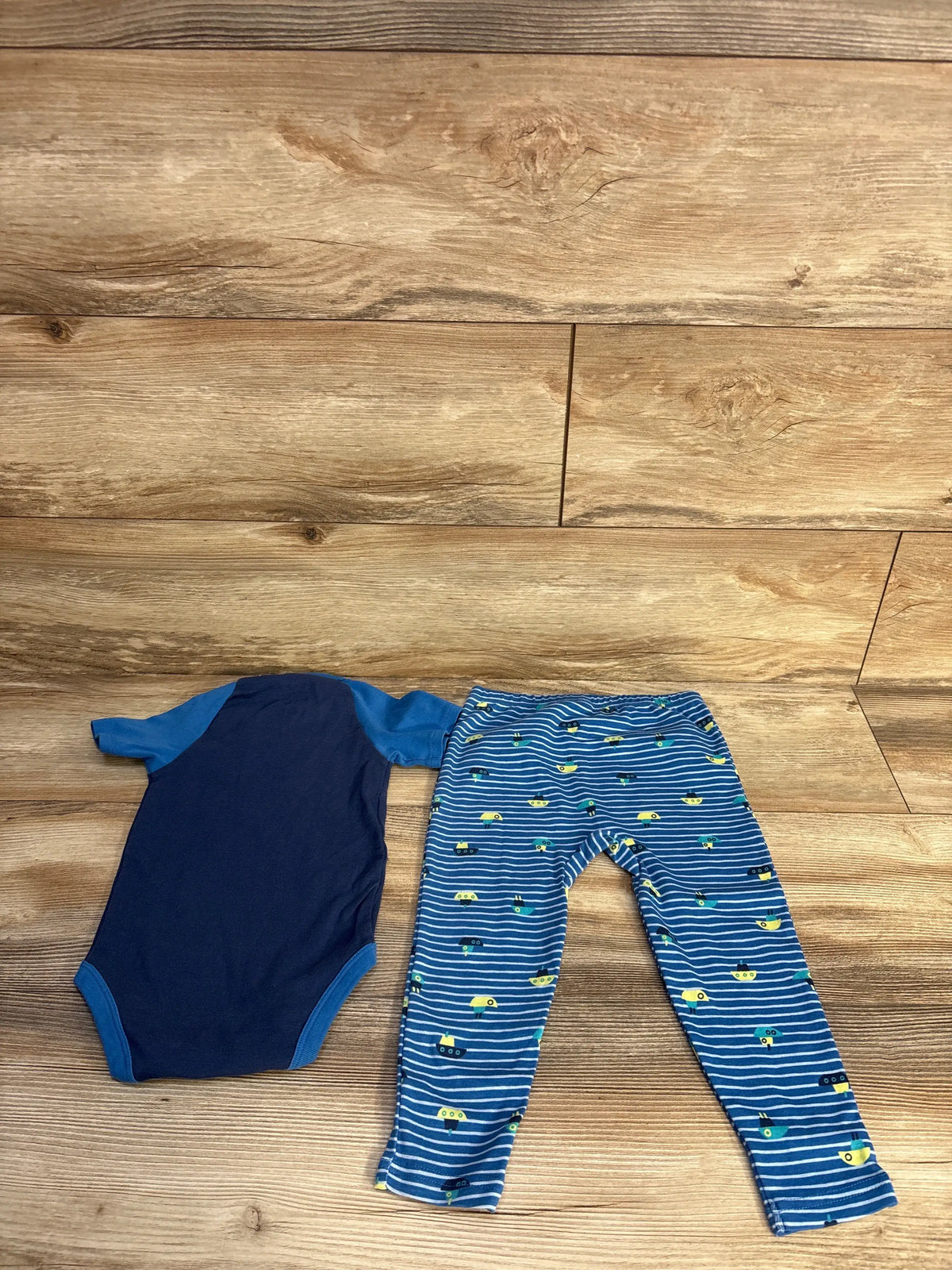 Top view of Okie Dokie Daddy’s First Mate bodysuit and pants set showcasing blue submarine print on pants with wood background