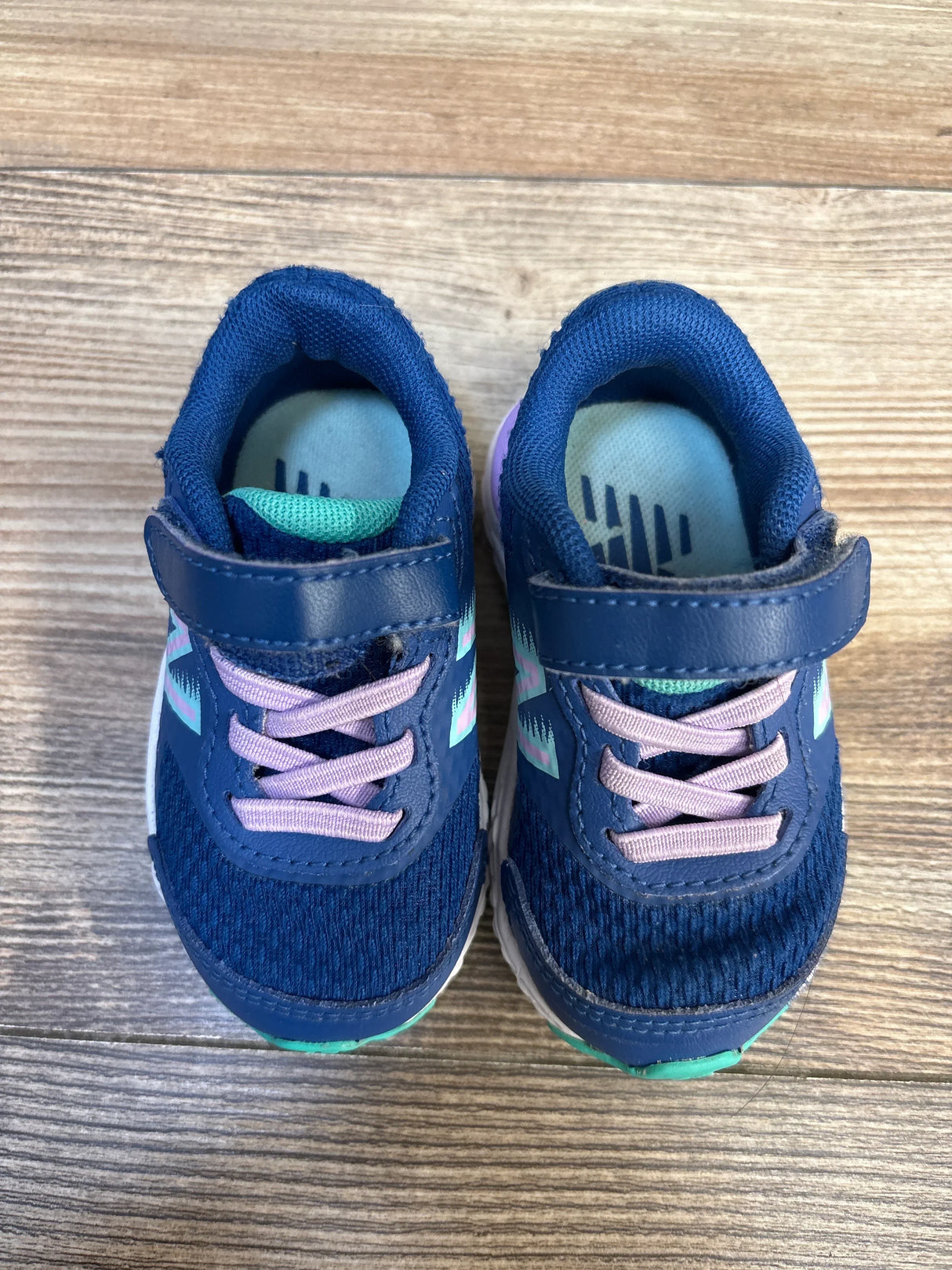Navy blue toddler sneakers with purple laces and Velcro straps on wood floor