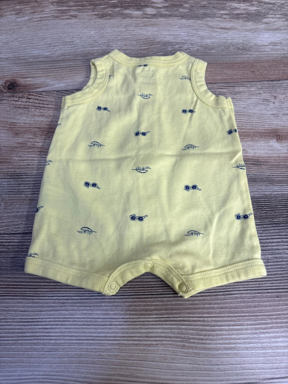 Top view of yellow Carter's shortie romper showing small navy sunglasses print and snap crotch on wood background