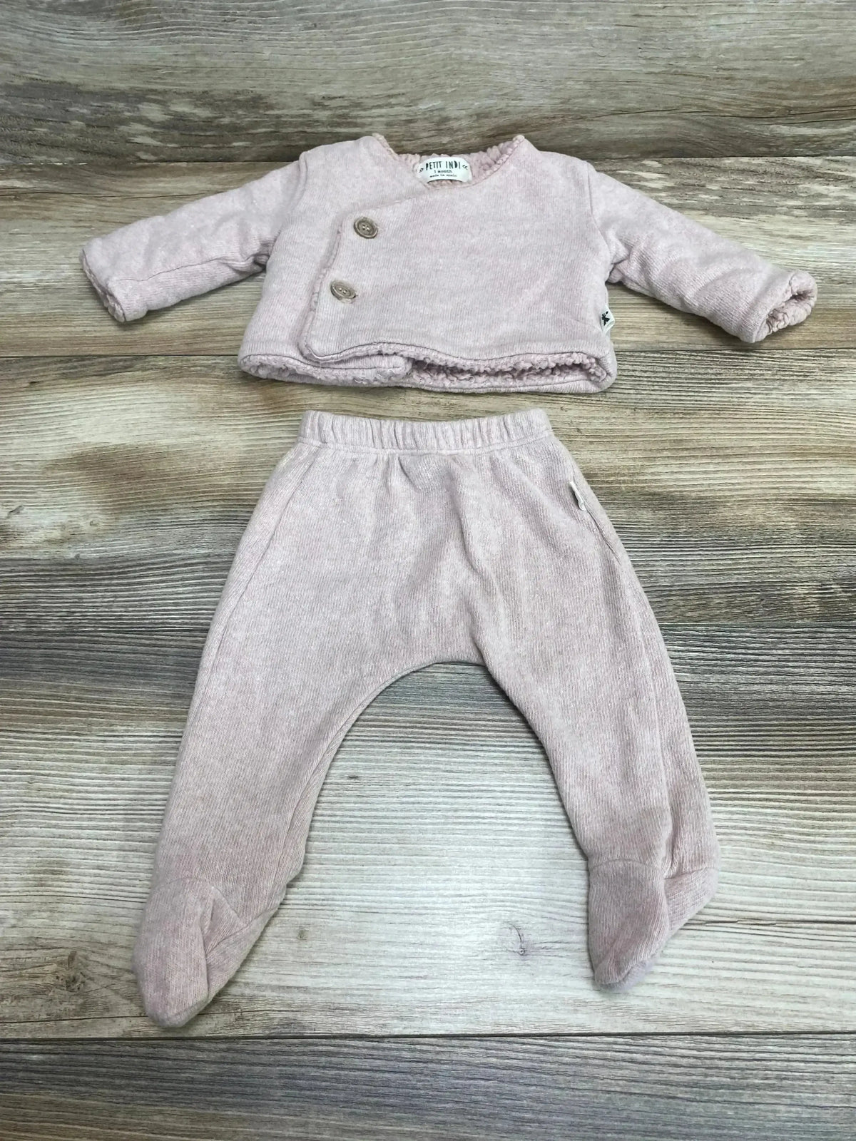 Flat lay of Petit Indi 2-piece pink organic baby set with double-button jacket lined in sherpa and matching footed pants on wooden background