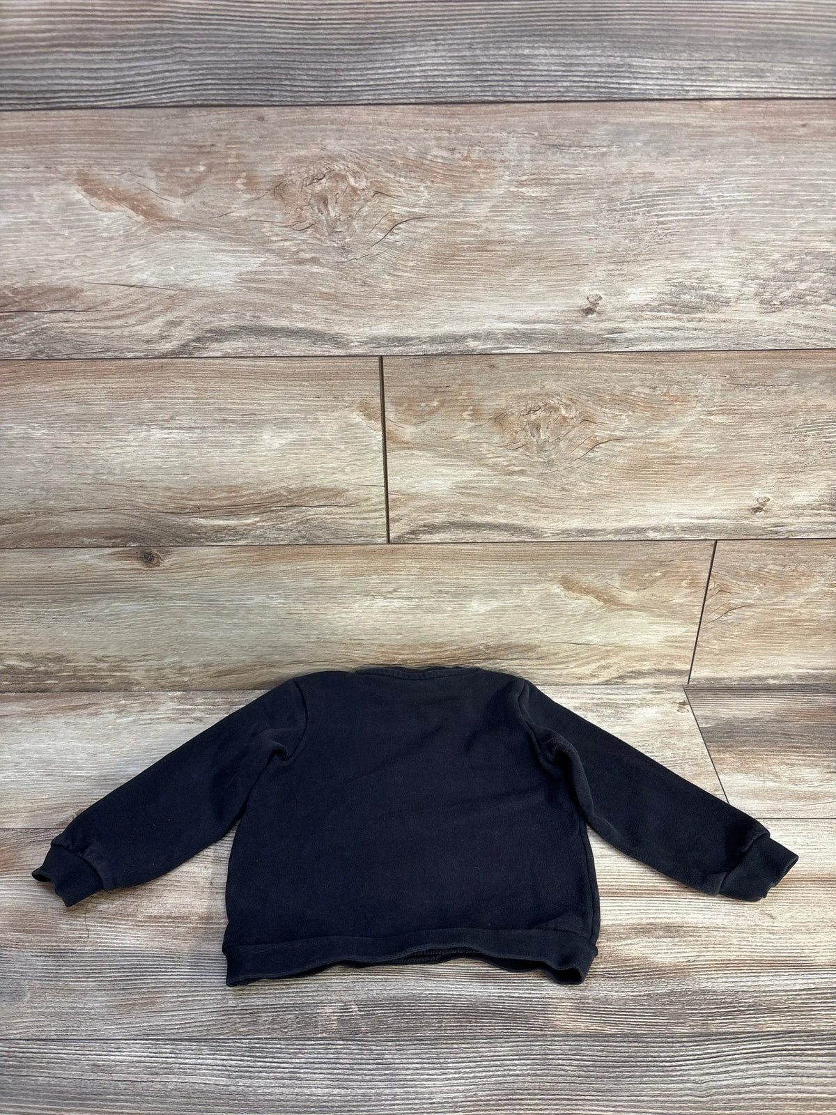 Front view of a black Puma pullover sweatshirt in size 2T showcasing its relaxed fit with a wood-look background