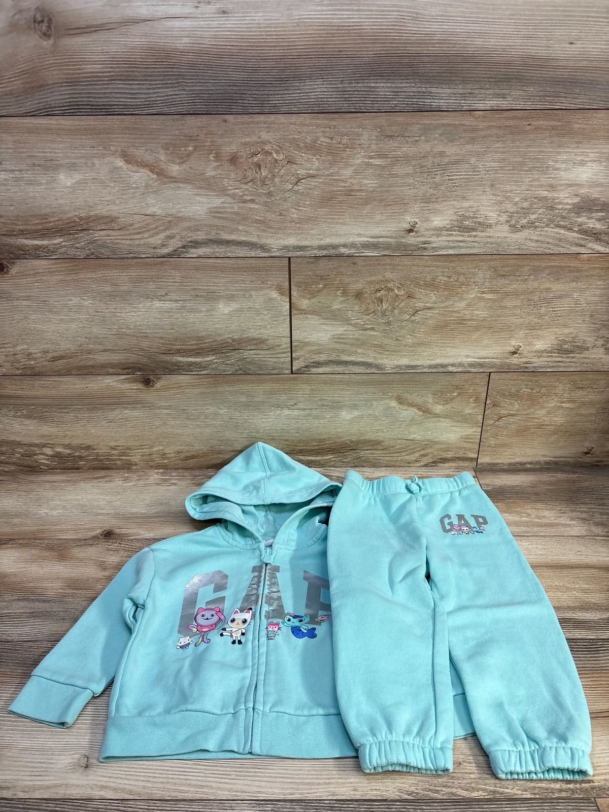 Top view of Baby Gap 2 piece zip up sweatshirt and joggers set in blue showcasing GAP graphics on a wood backdrop