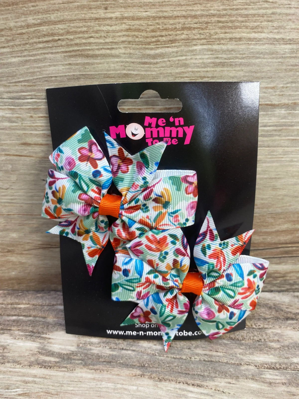 Front view of two floral green fanned out hair bows with colorful floral patterns on black packaging