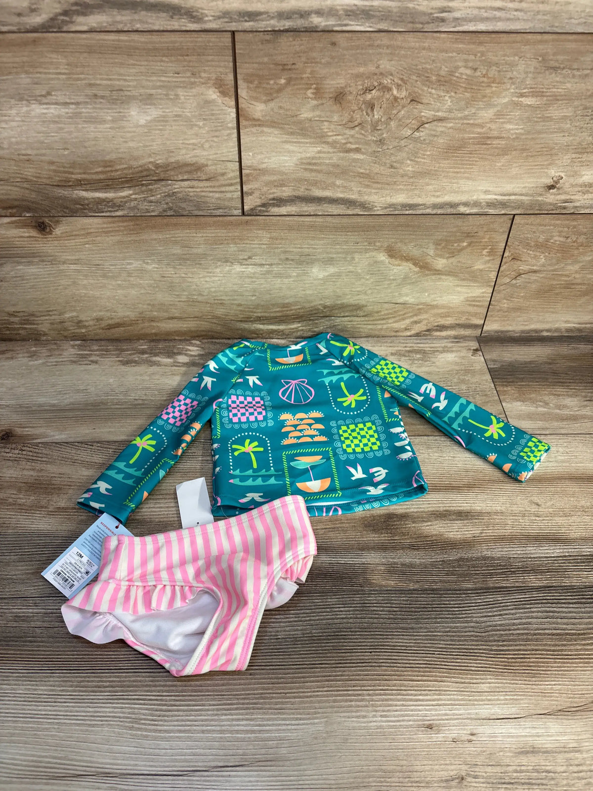 Flat lay of Cat and Jack toddler rashguard tankini showing seafoam long-sleeve top and pink striped ruffle bottoms on wood
