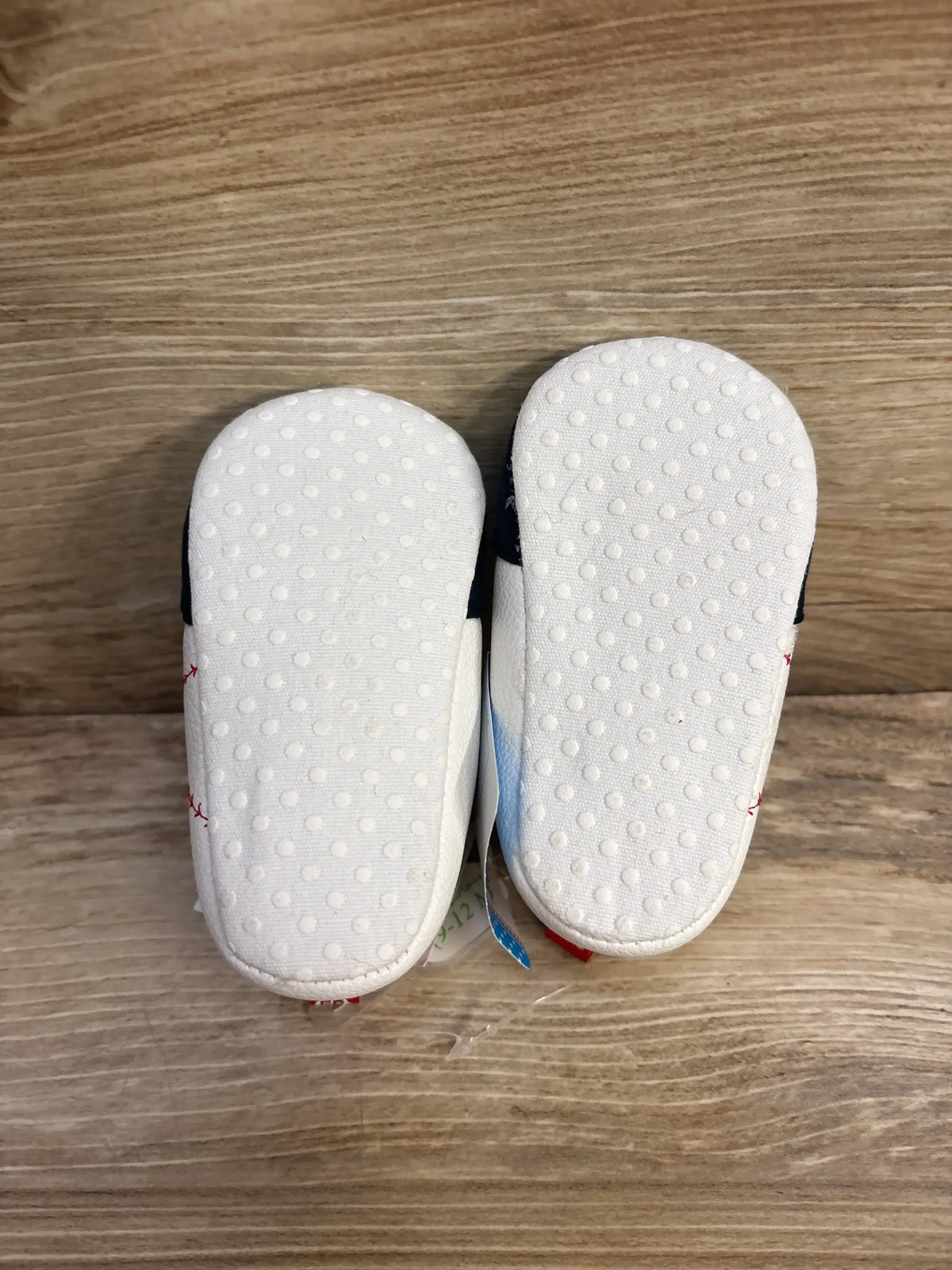 Bottom view of Stepping Stones baby baseball shoes size 9–12 months showcasing white dotted non-slip soles on wood background