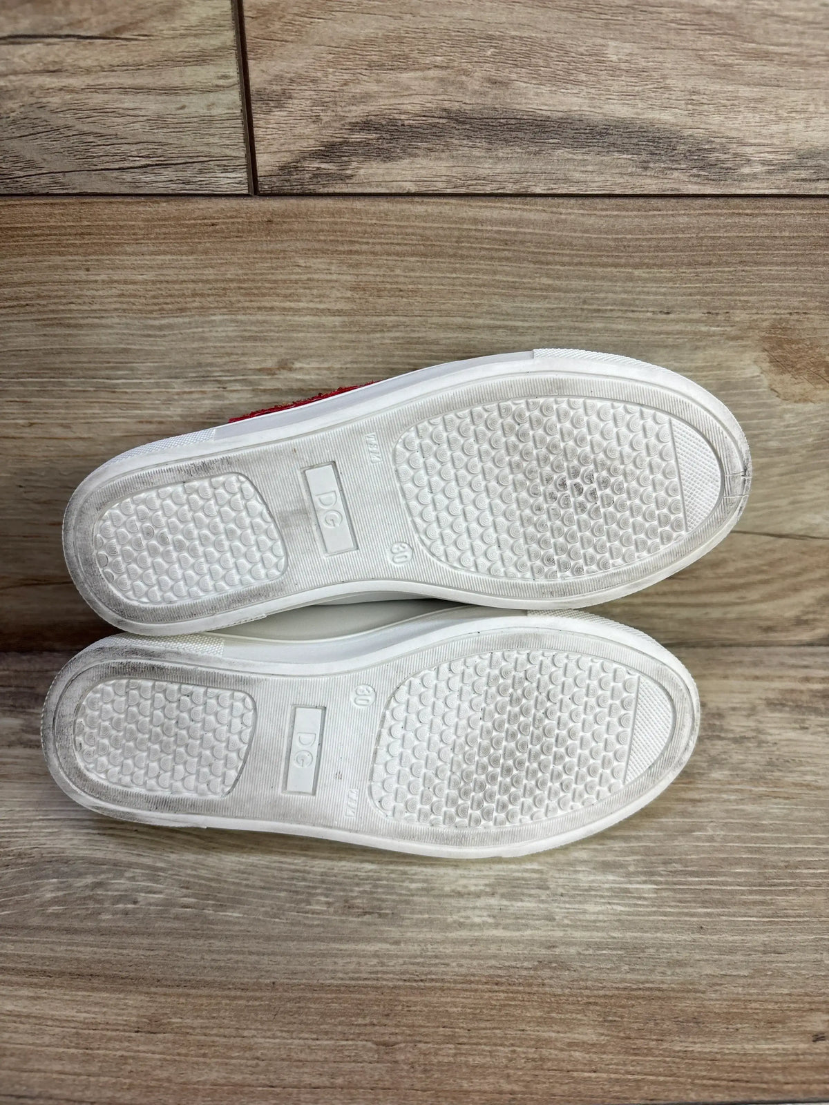 Underside view of white Portofino DG Amore sneakers showcasing textured branded rubber soles on a wood surface