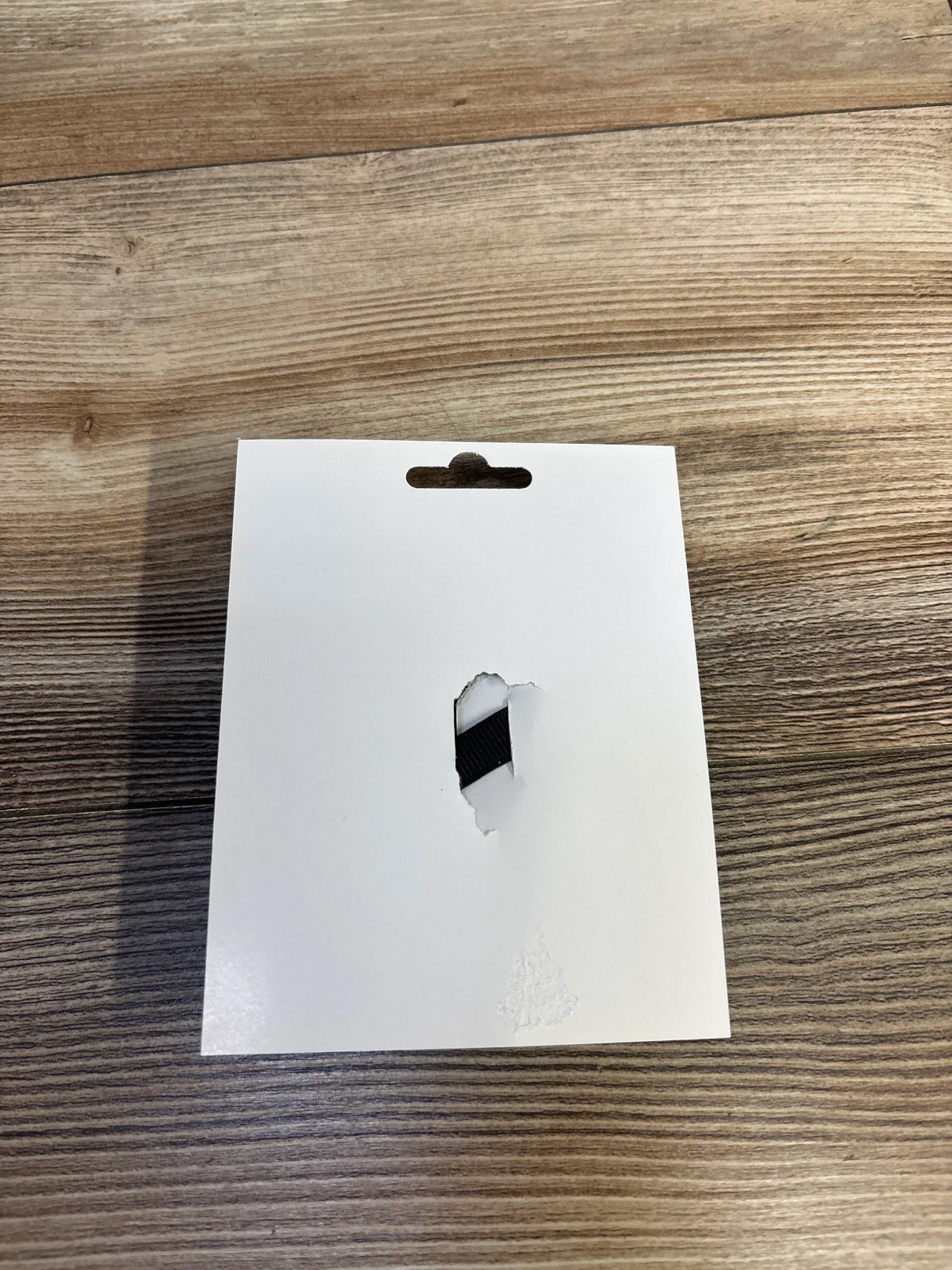 White product tag with torn hole revealing black ribbon, on wooden surface