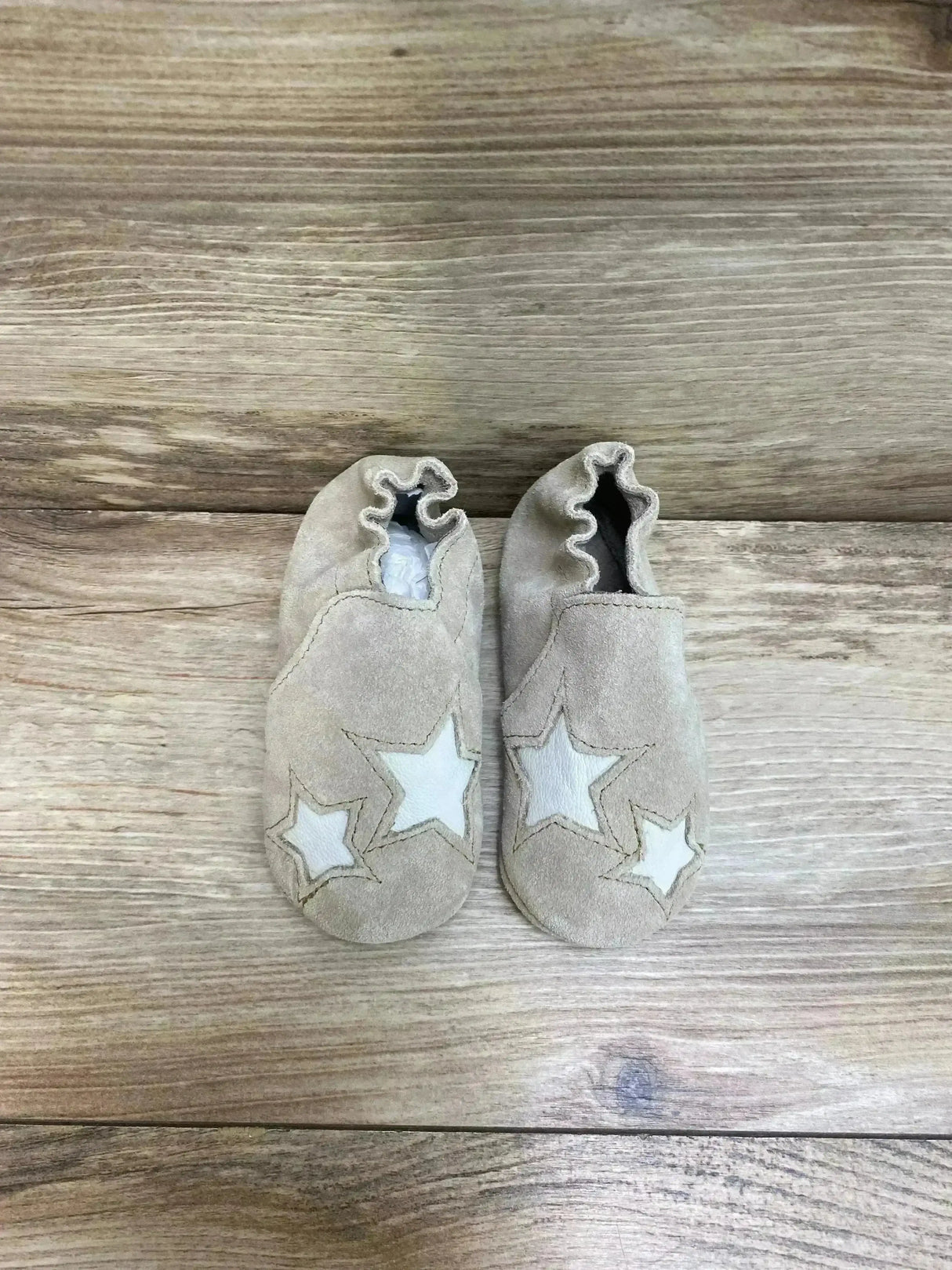 Top view of Minnetonka Star infant booties tan suede with elasticized ankles and white star appliques on wood background