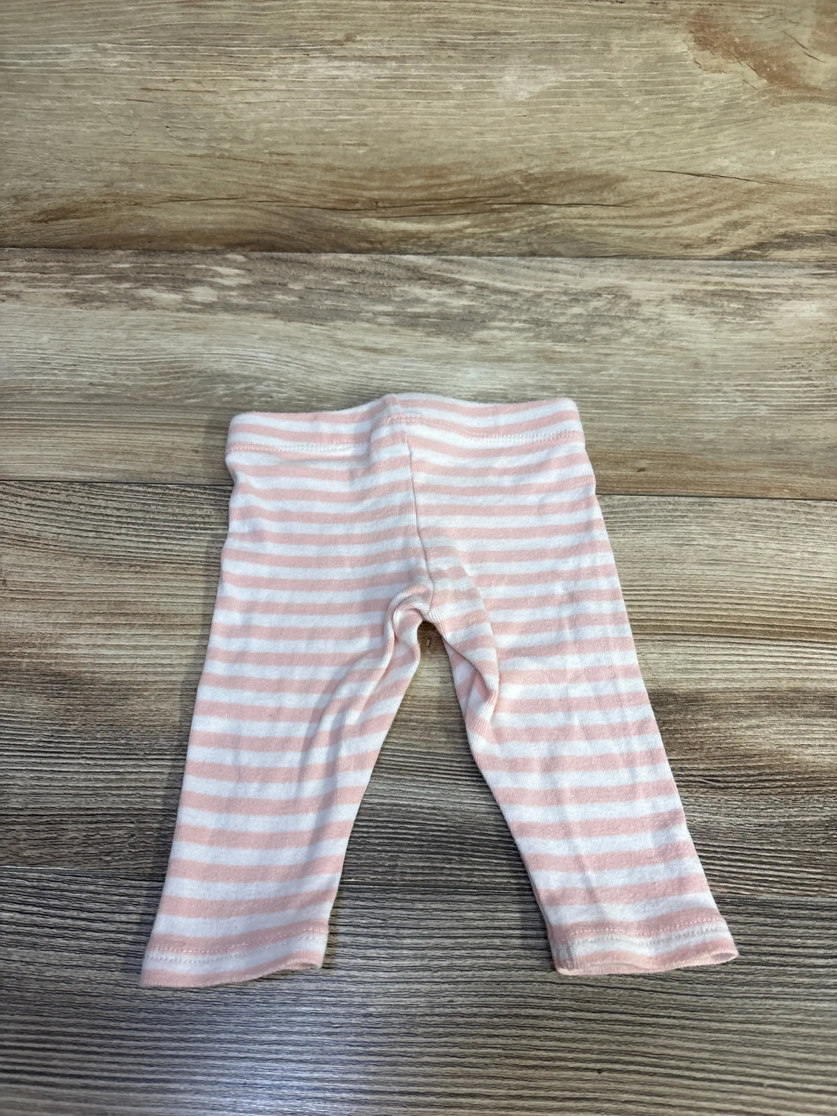 Top-down view of pink and white striped baby leggings size 3-6 months showing elastic waistband on wood surface