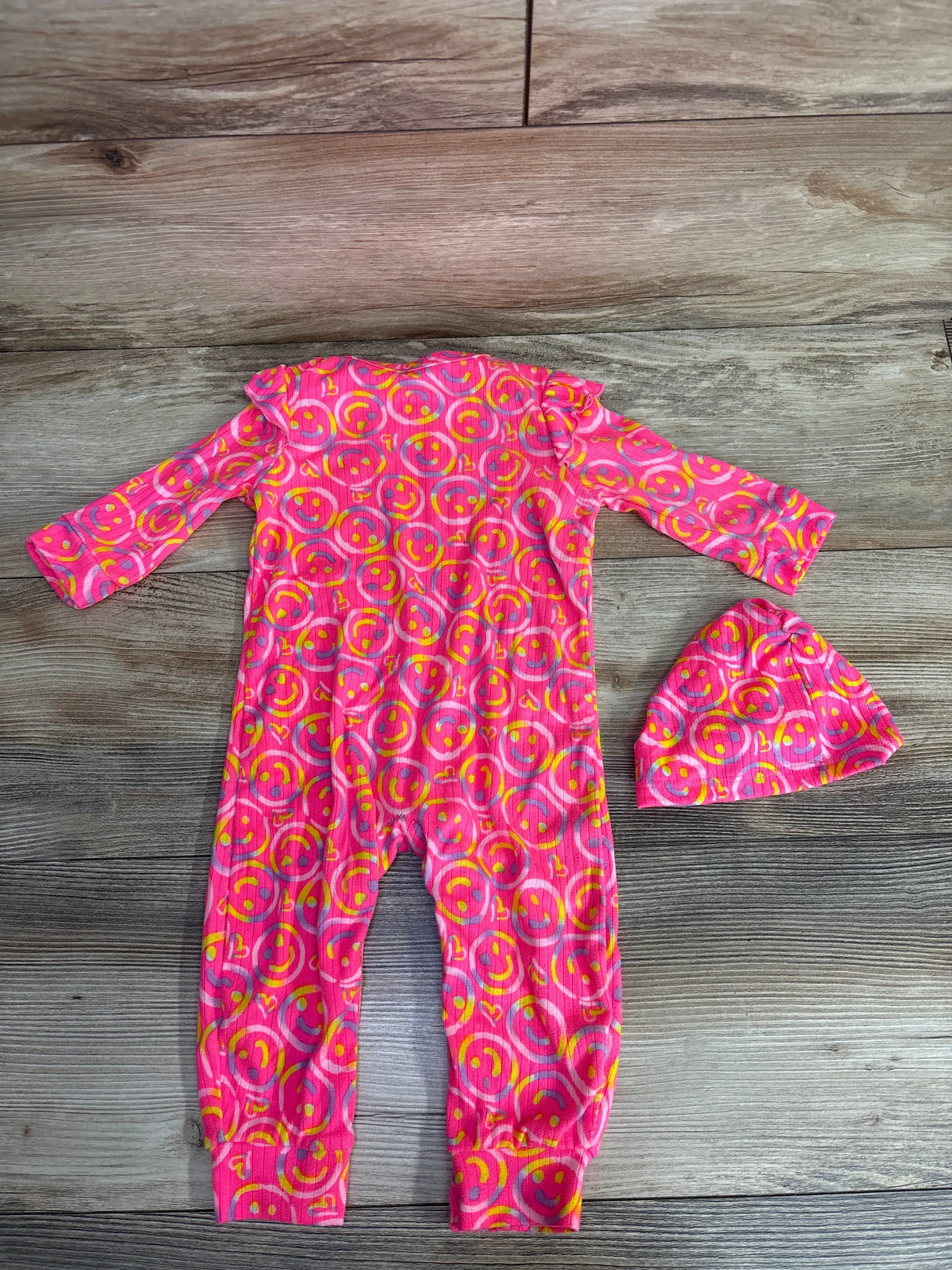 Pink baby romper and hat set with yellow smiley face print on wooden floor