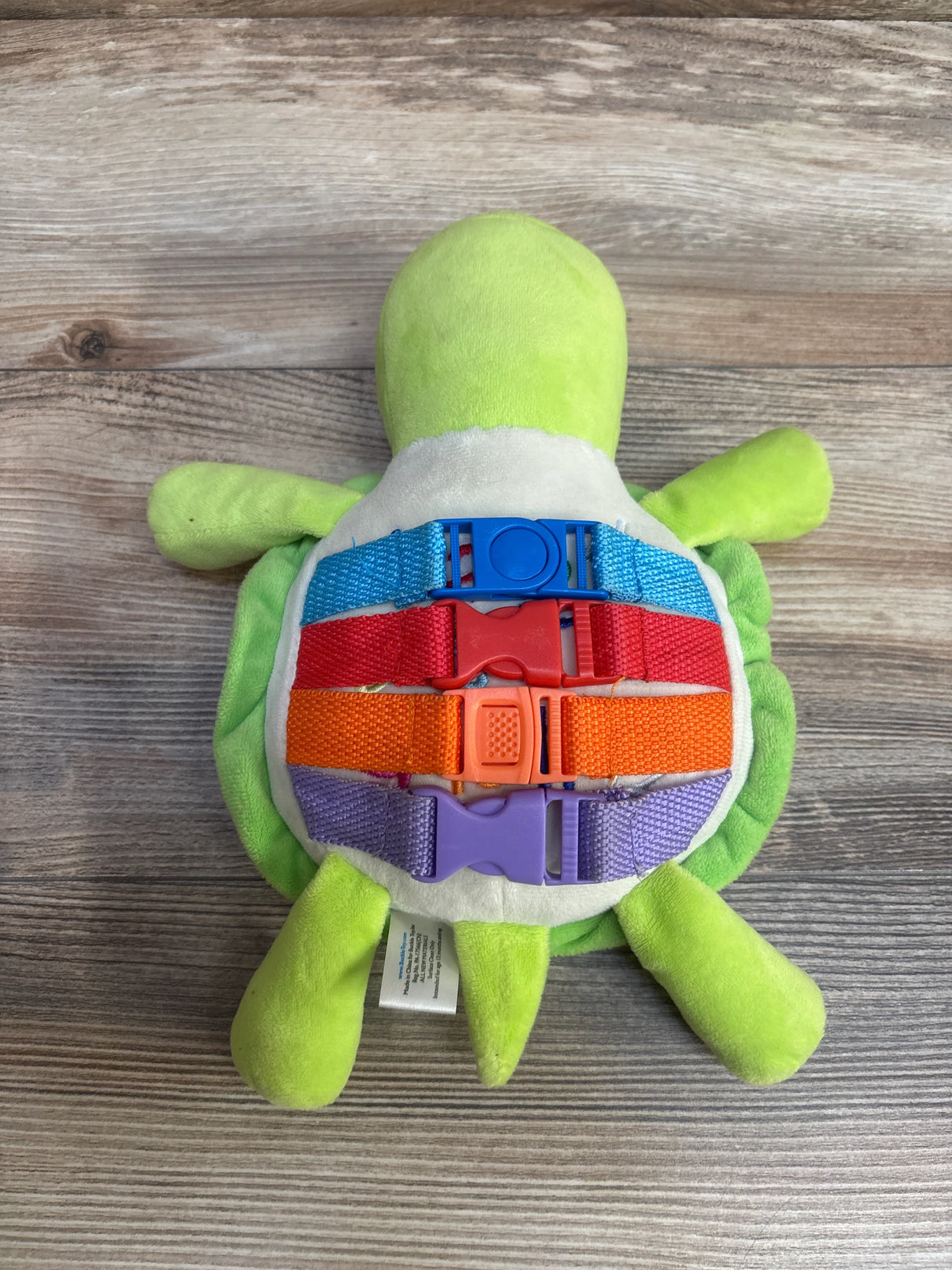 Plush turtle toy with colorful buckle straps on shell, on wood background