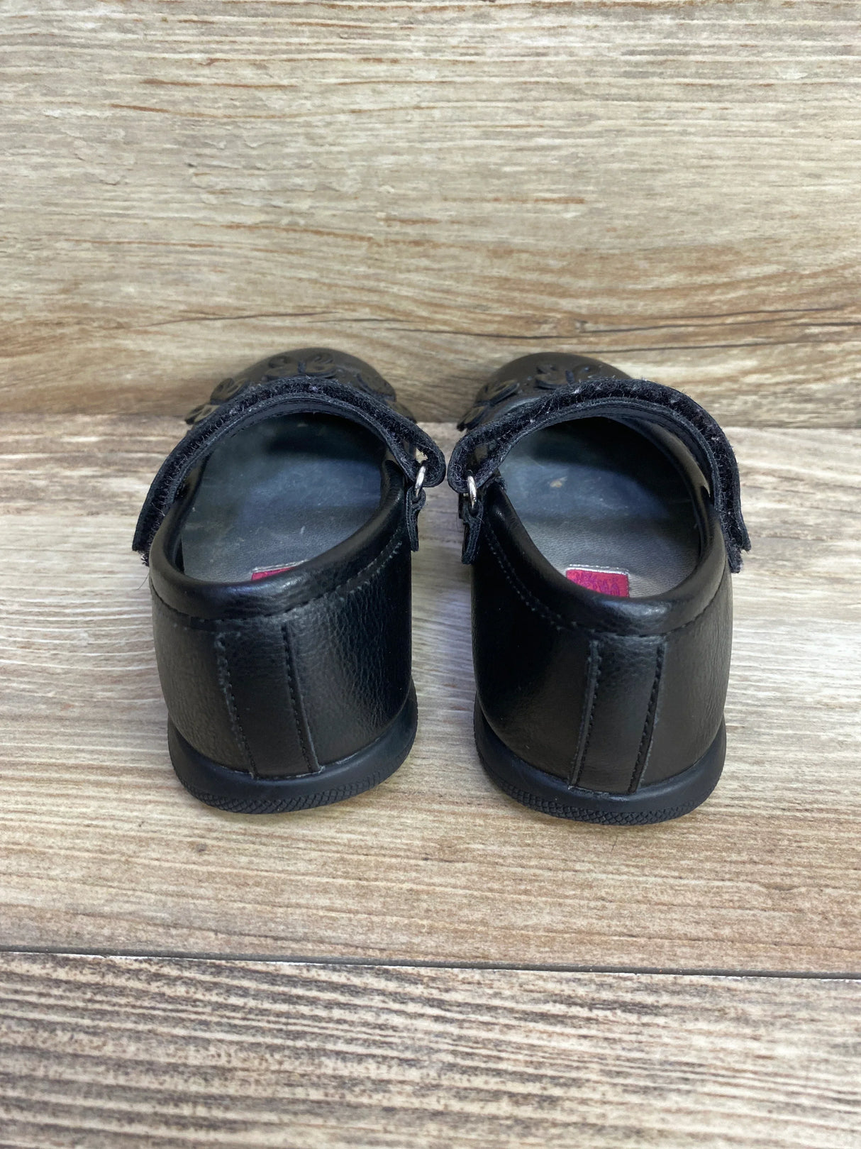 Back view of a pair of black leather toddler shoes with Velcro straps on wood floor