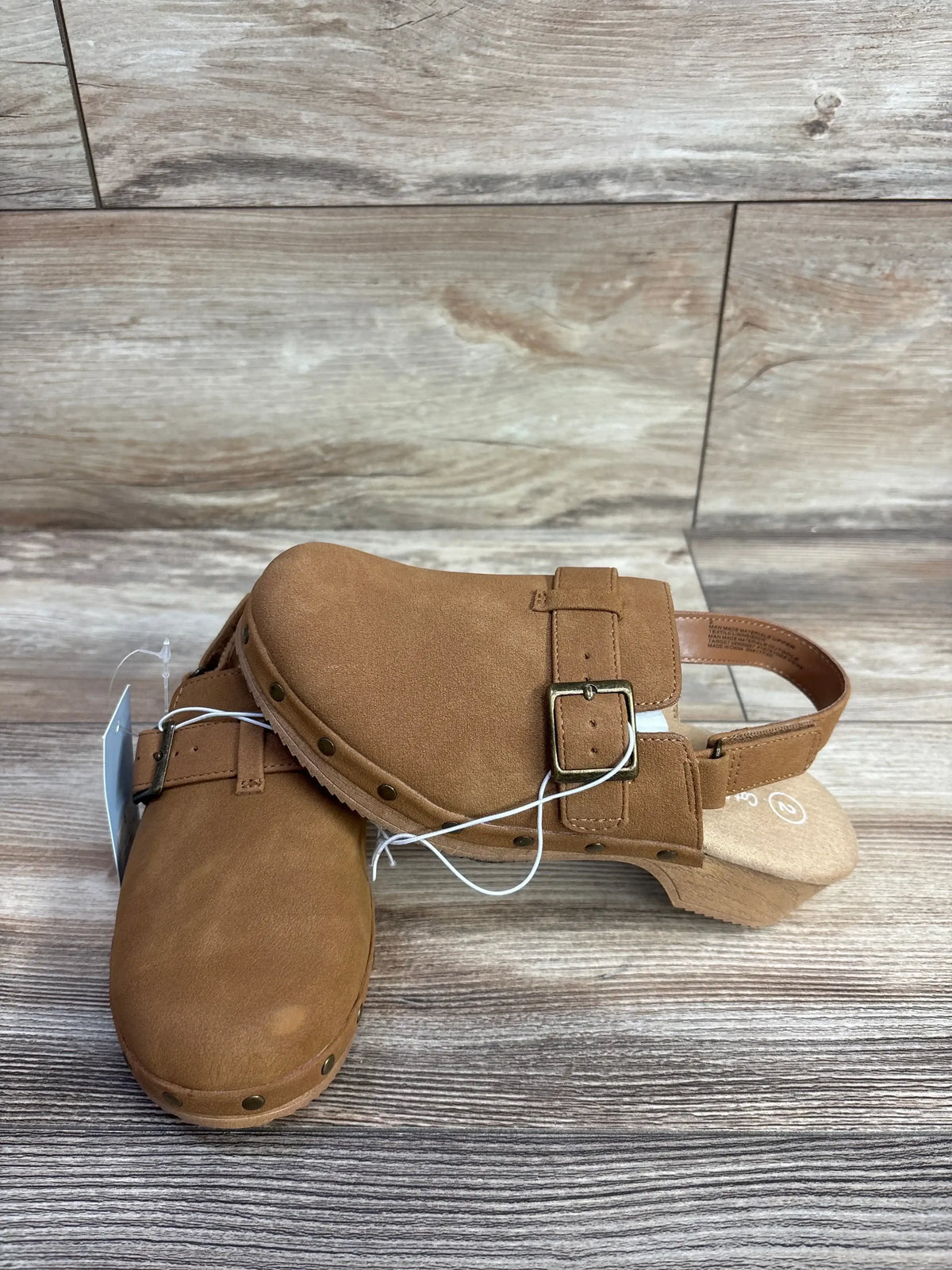 Pair of kids brown faux suede clogs with adjustable buckle strap on wood floor