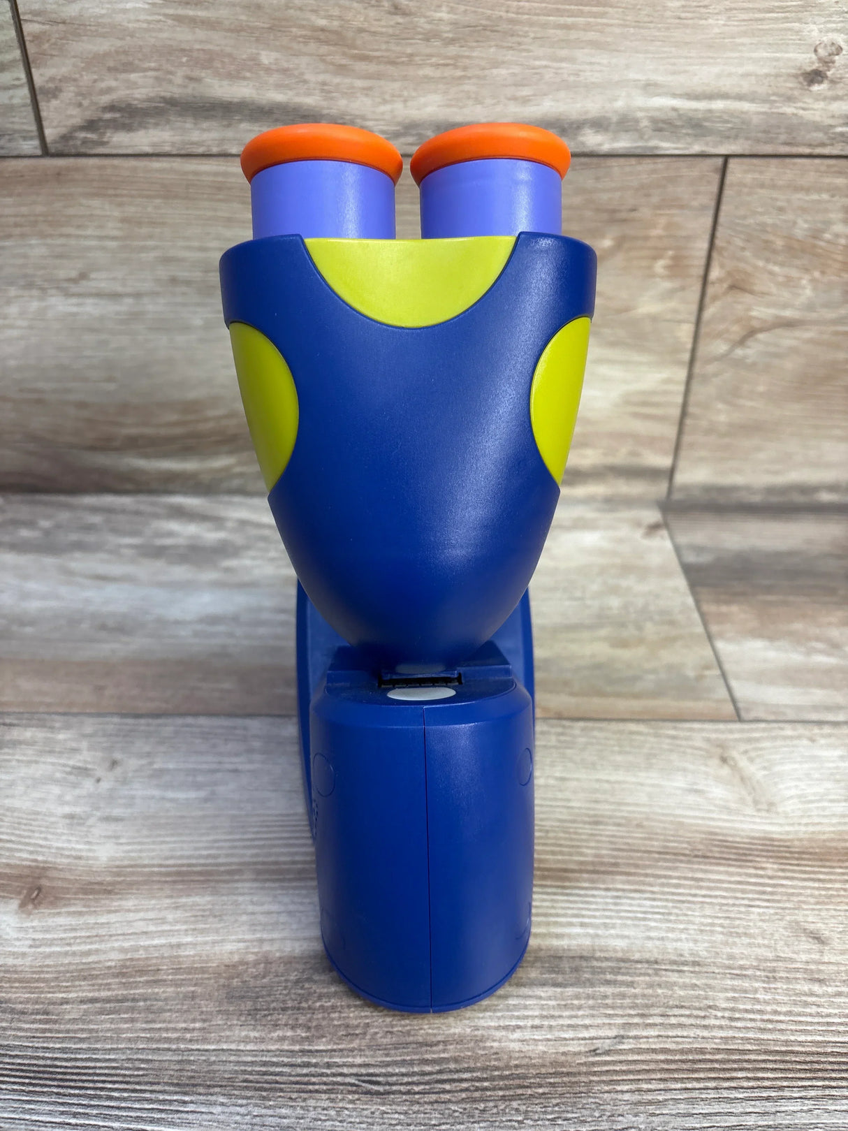Front view of GeoSafari Jr. microscope with blue body, green accents and orange tipped purple eyepieces on wood background