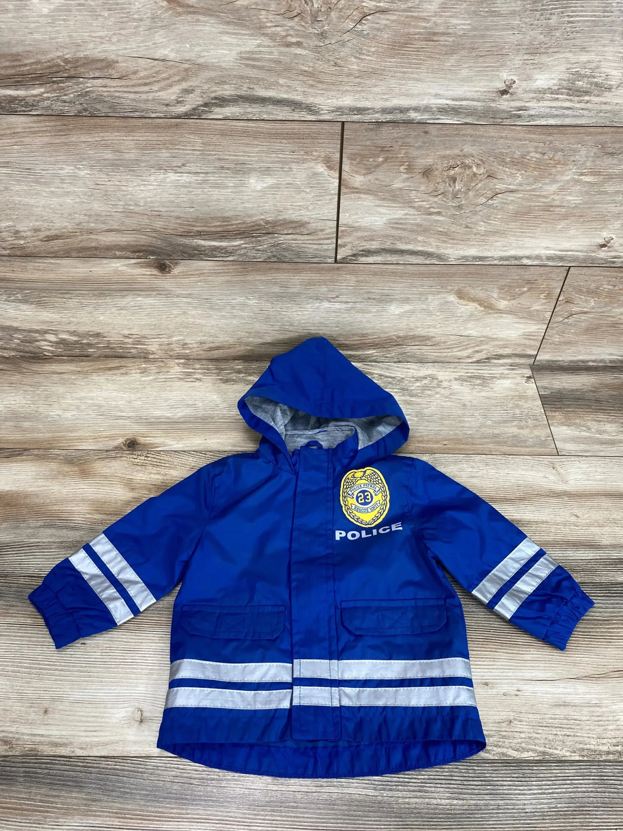 Front view of blue toddler hooded windbreaker with reflective silver sleeve and hem stripes and POLICE badge on wood floor