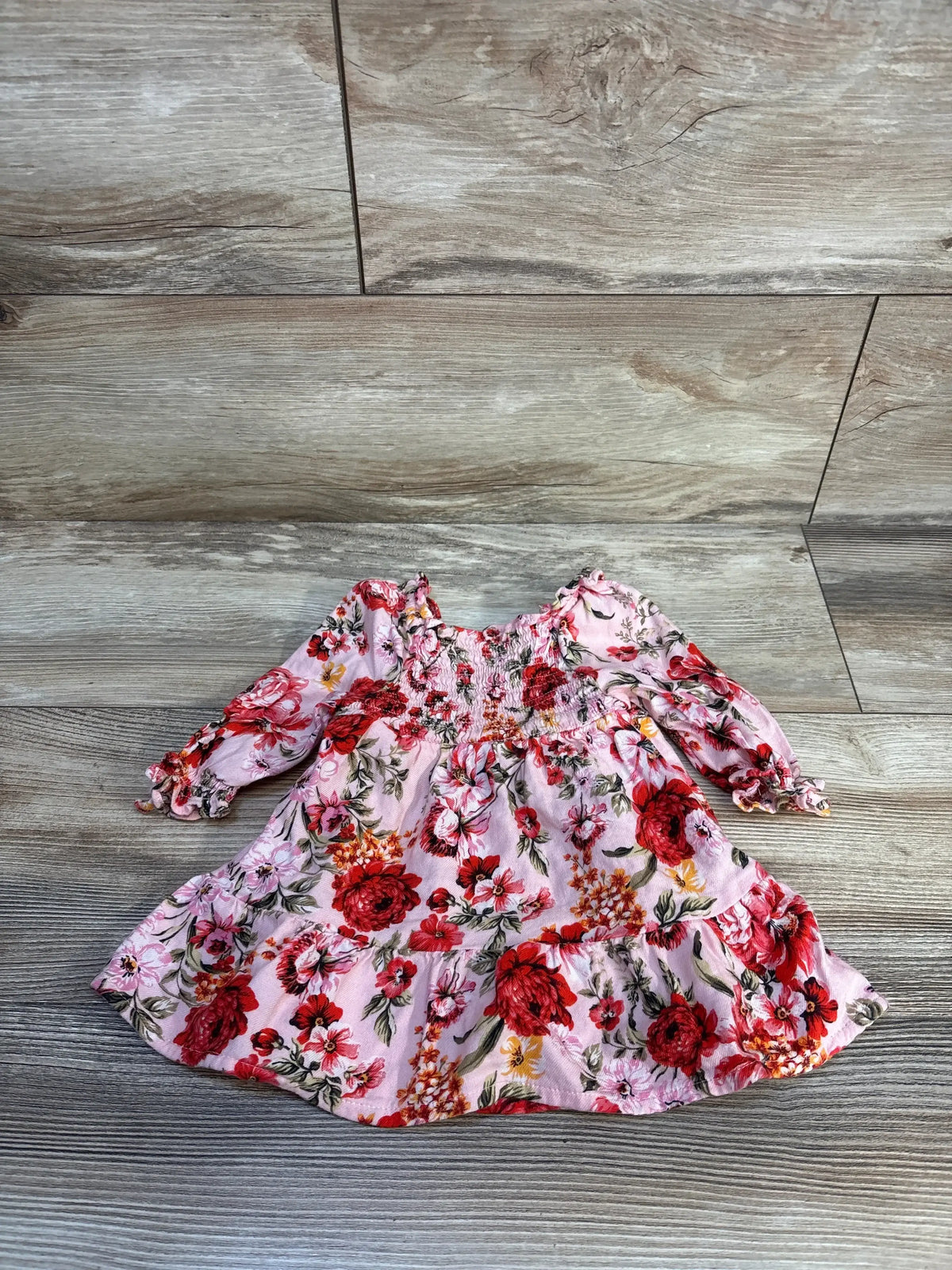 Pink long sleeve baby dress with red floral print on a wood floor