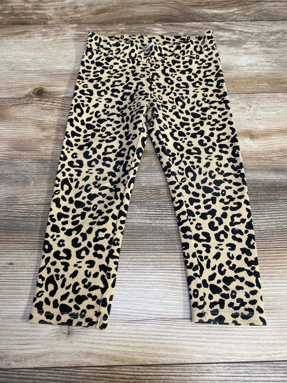 Flat lay of Janie and Jack toddler leggings showing beige leopard print and elastic waistband on wood floor