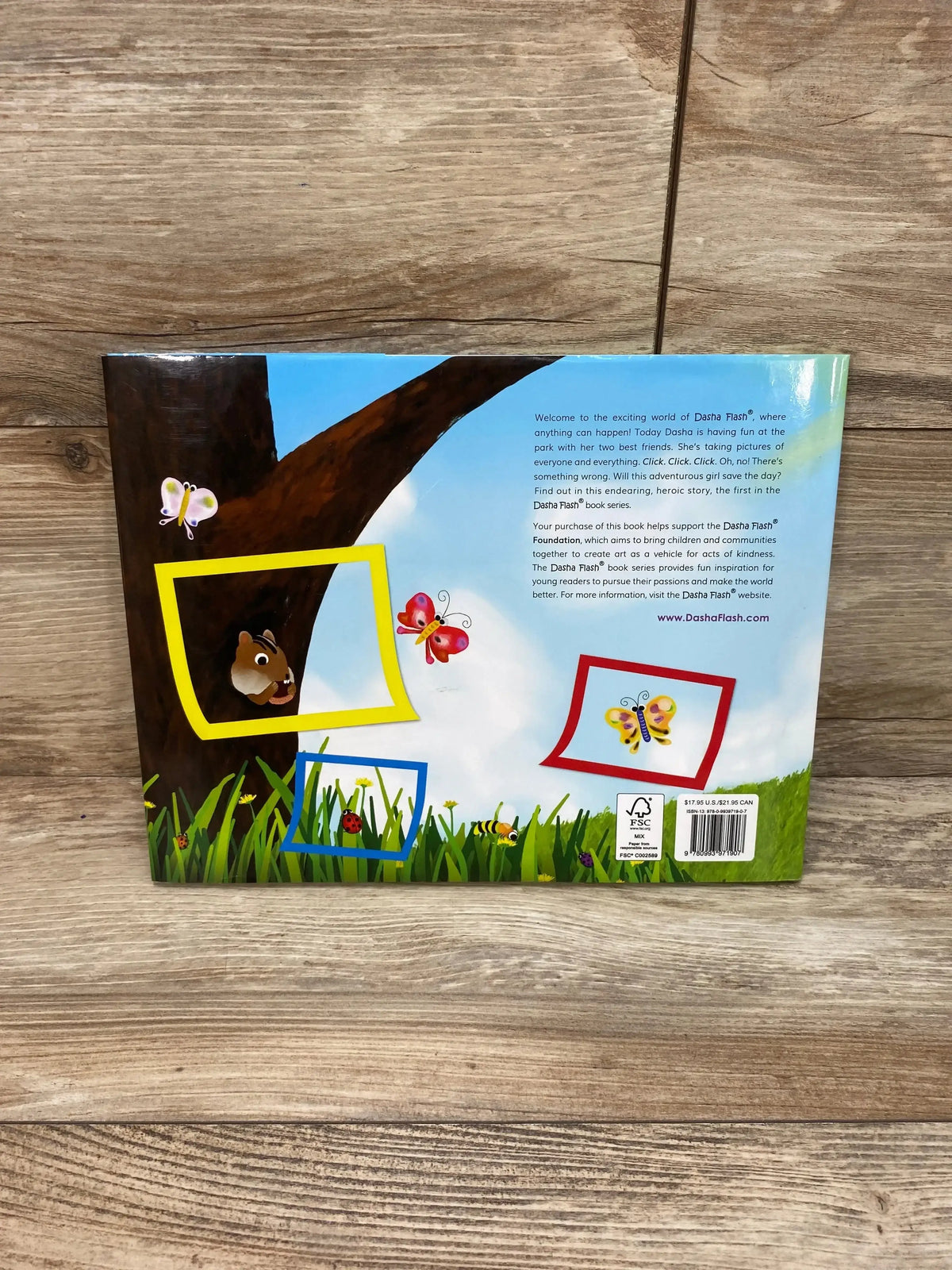 Back cover of Dasha Saves the Day: At the Park book showing tree and butterflies, photo-frame cutouts and barcode on wood surface