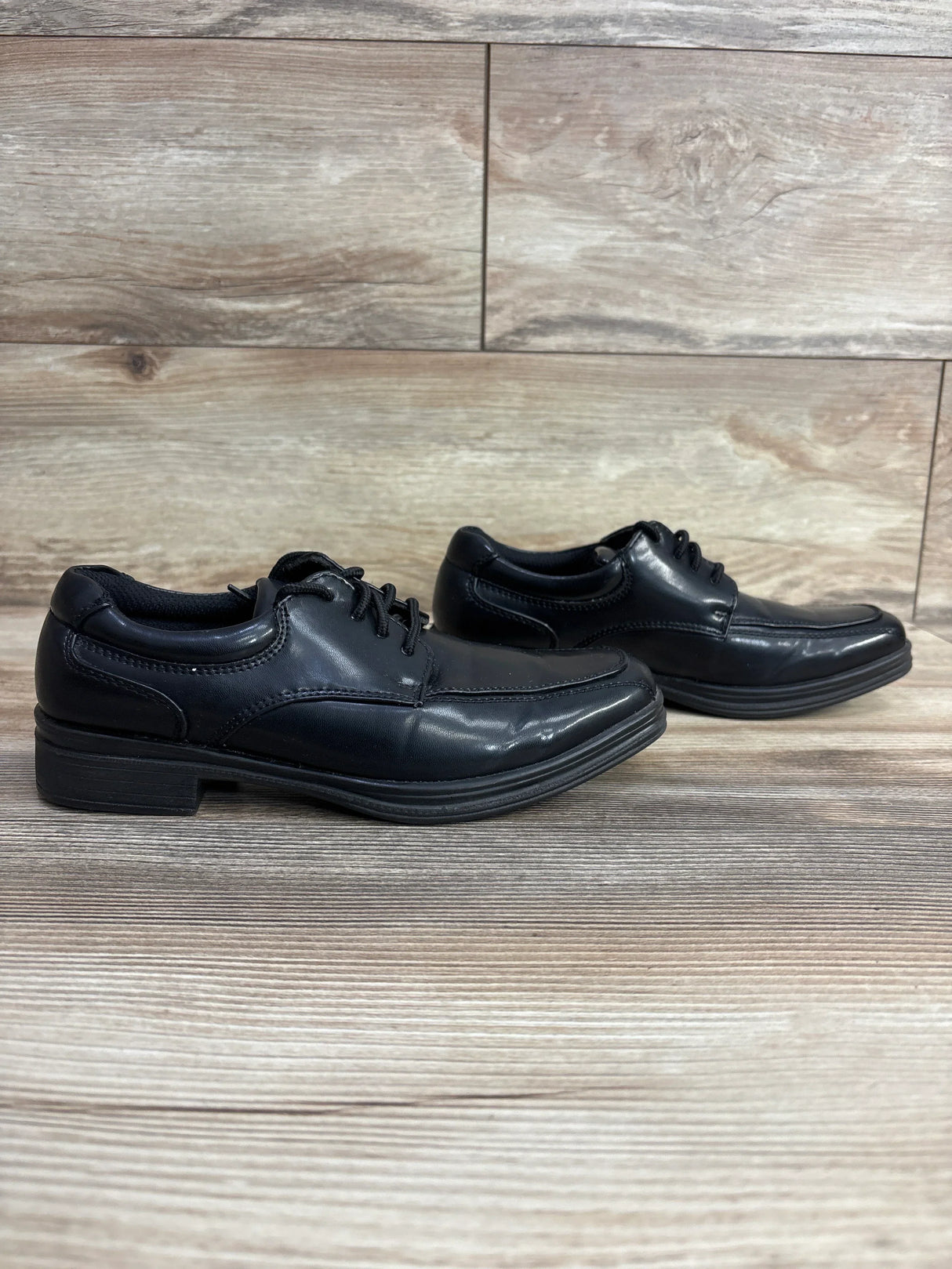 Pair of black leather children's dress shoes with laces on wooden floor background