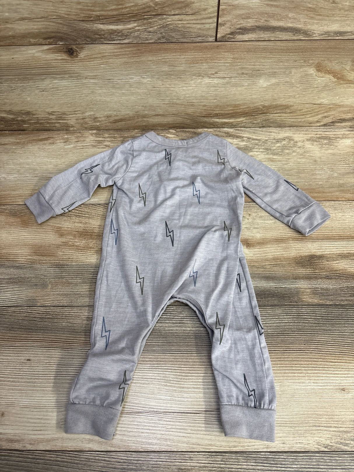 Gray baby onesie with long sleeves and multicolor lightning bolt prints on wood floor