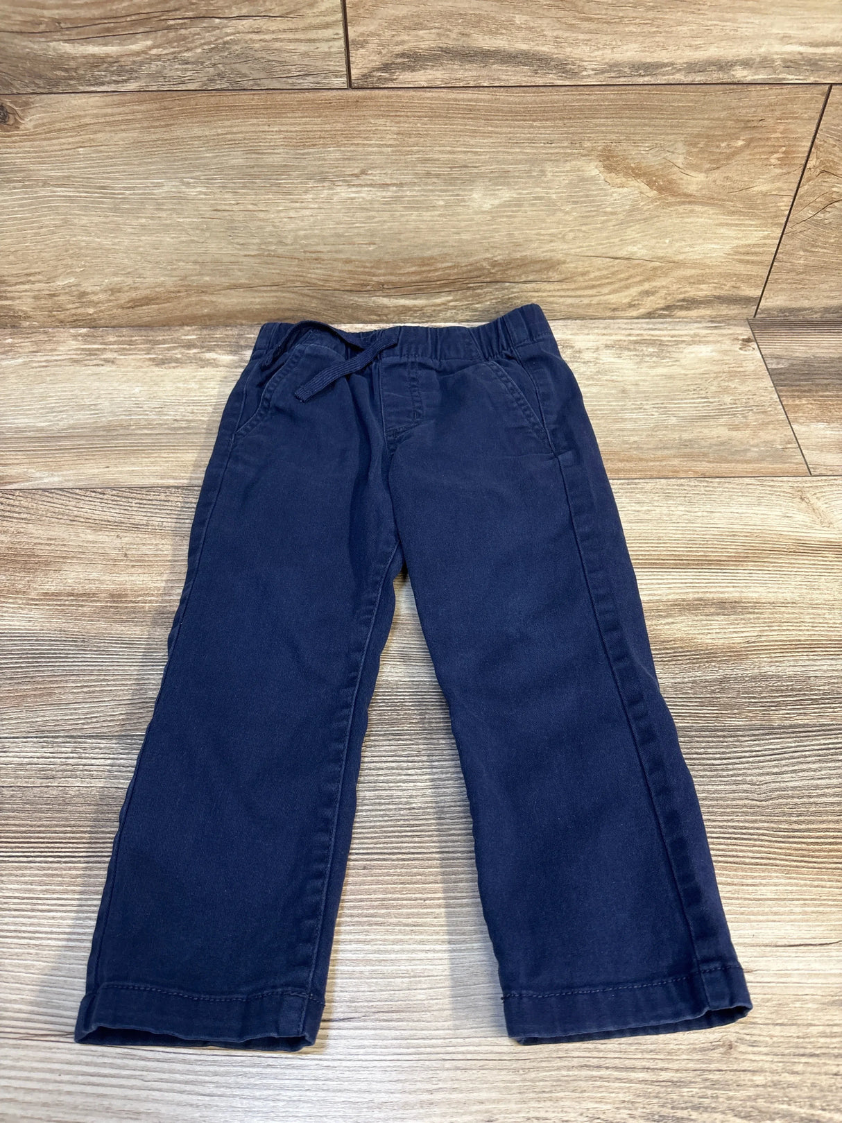 Flat-lay front of navy toddler twill pants with elastic drawstring waistband and side pockets on wood background