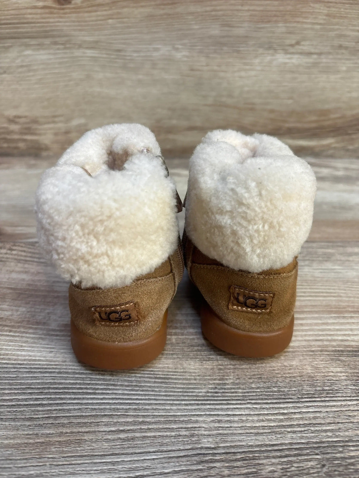 Pair of toddler brown suede UGG boots with white shearling lining on wood floor