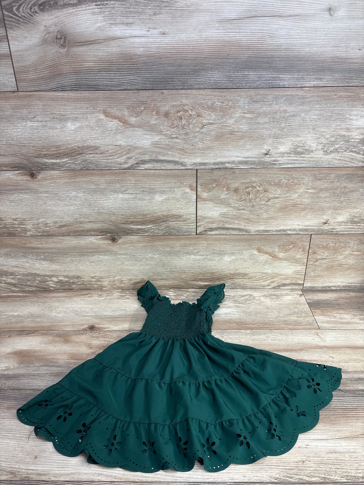 Dark green tiered girls dress with smocked bodice and eyelet scalloped hem on wood floor
