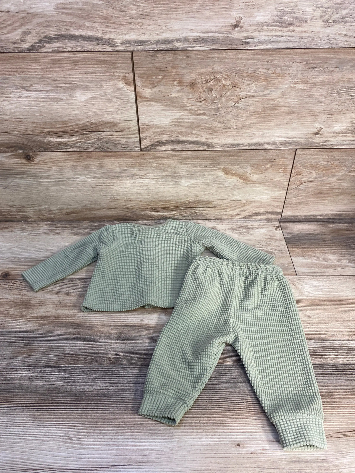 Flat lay of Rabbit Moon green textured shirt and pants set for size 0-3 months on a wood-look floor