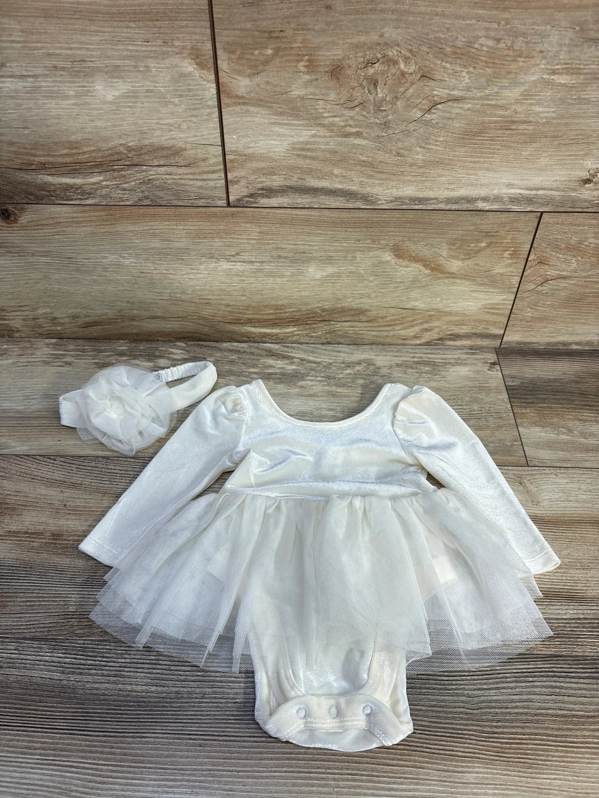 Front view of ivory velvet tulle bodysuit dress with puff sleeves, layered skirt, and matching flower headband on wood floor
