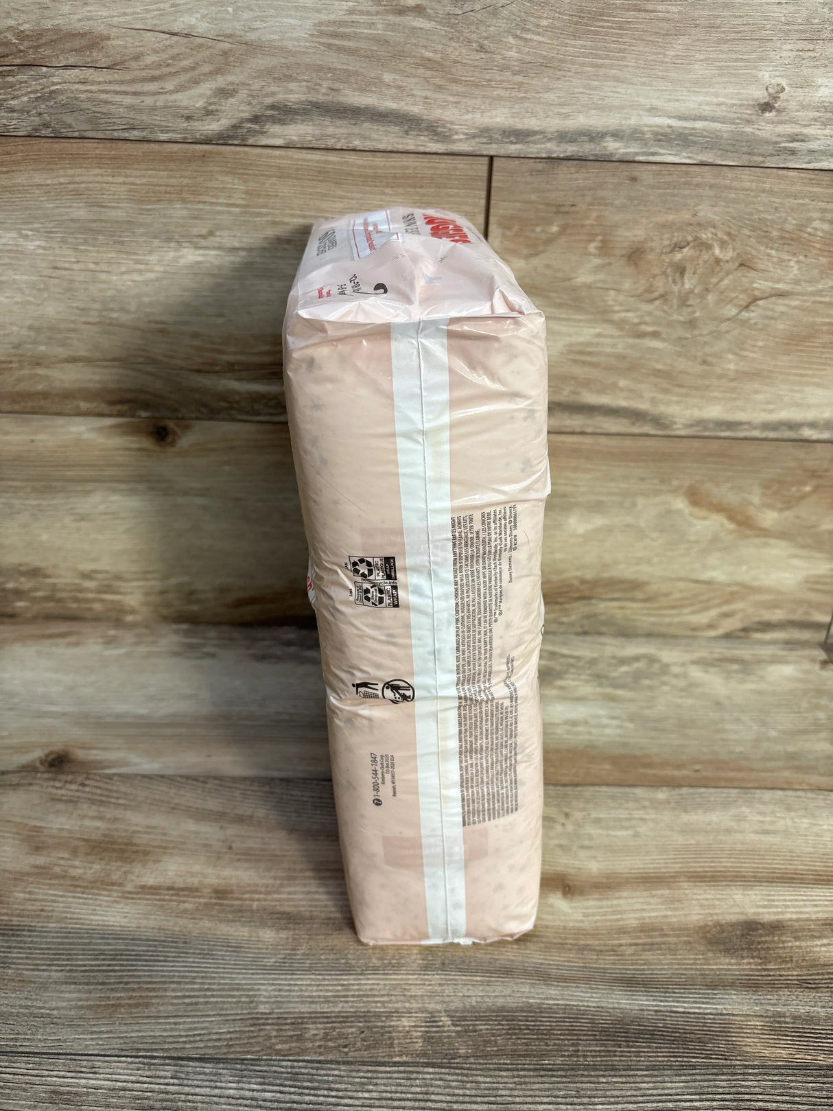 Pack of adult diapers on wooden floor, neutral packaging side view