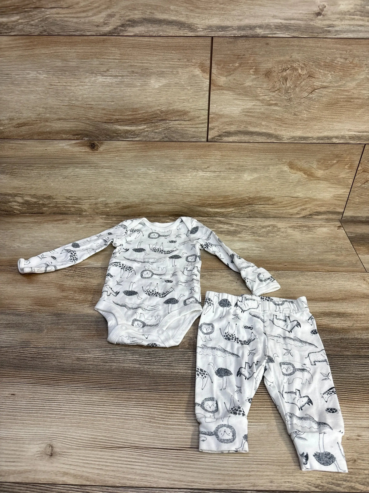 Flat lay of white long-sleeve animal-print baby bodysuit and matching pants showing gray animal sketches on a wood background