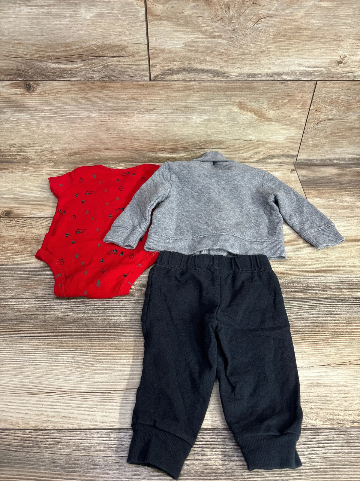 Baby boy outfit with red print onesie, gray sweater, and black pants on wood floor