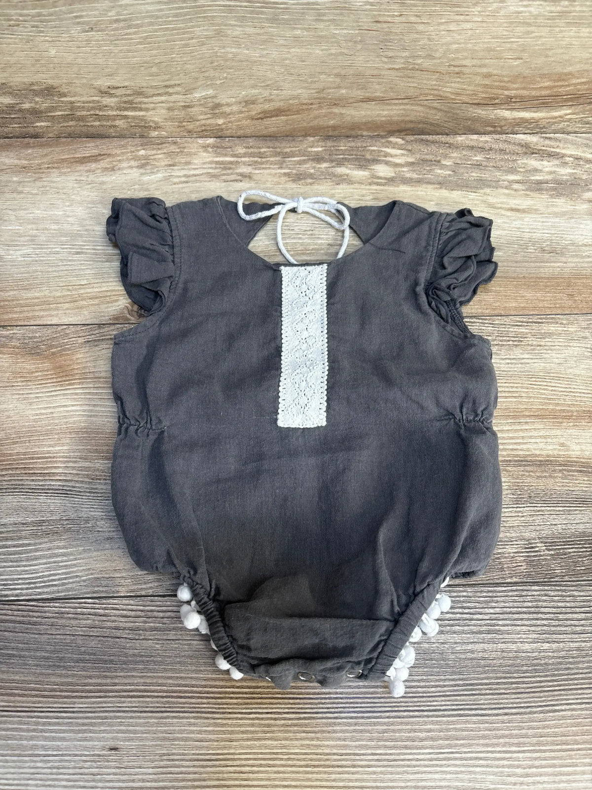 Gray baby romper with ruffled sleeves, white lace trim, and pom-pom hem on wood floor
