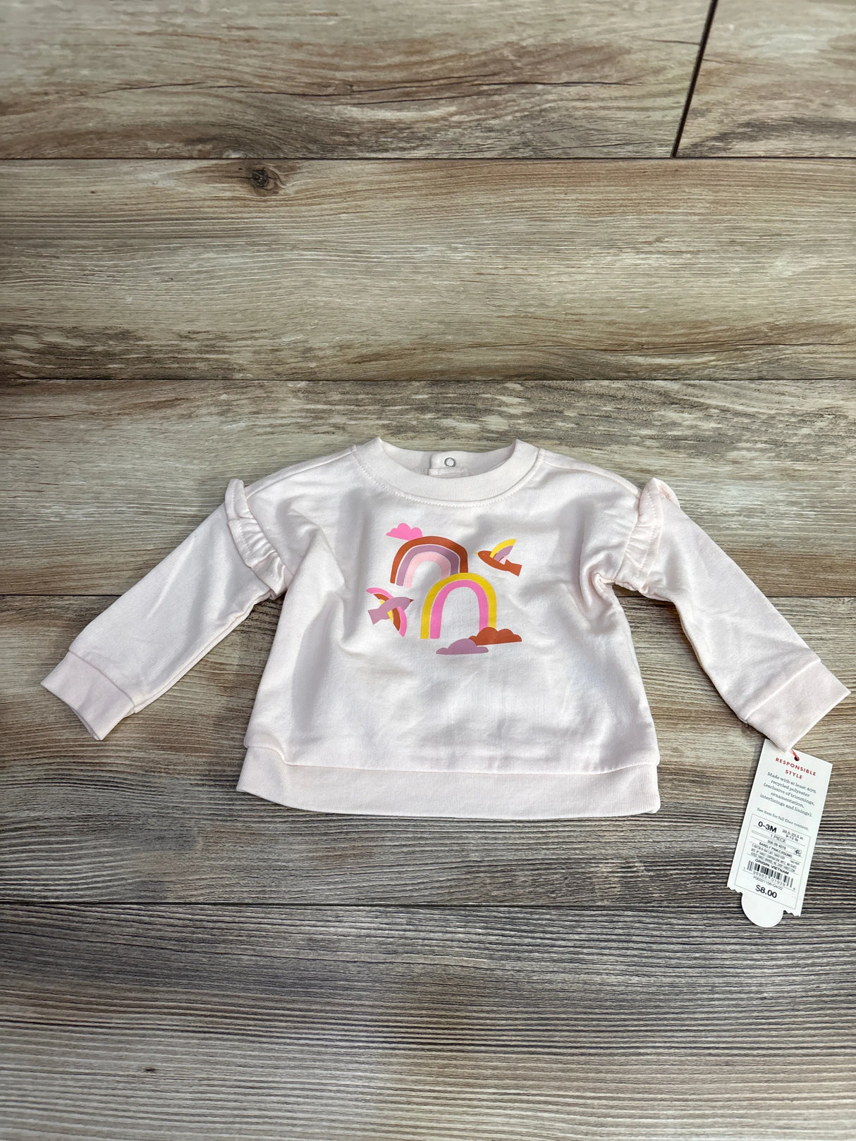 Pink baby sweatshirt with rainbow and birds print on wood floor, tag attached