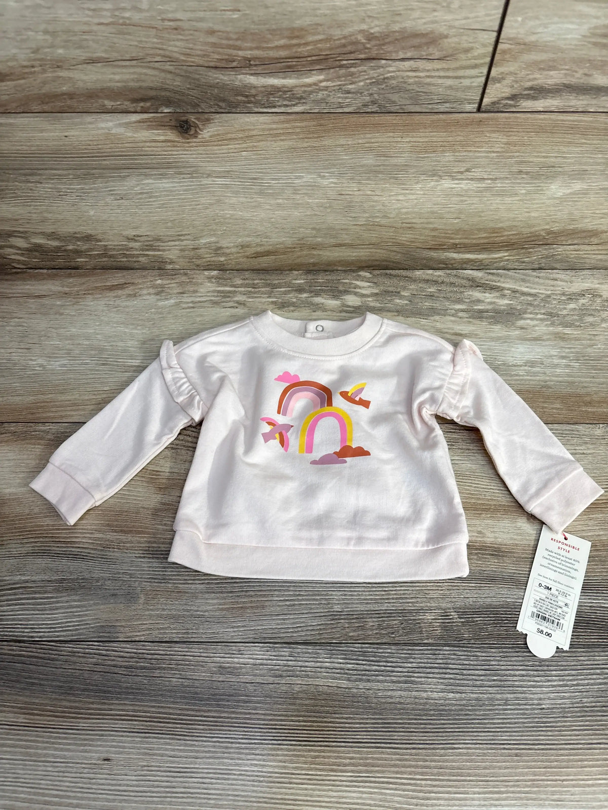 Pink baby sweatshirt with rainbow and birds print on wood floor, tag attached