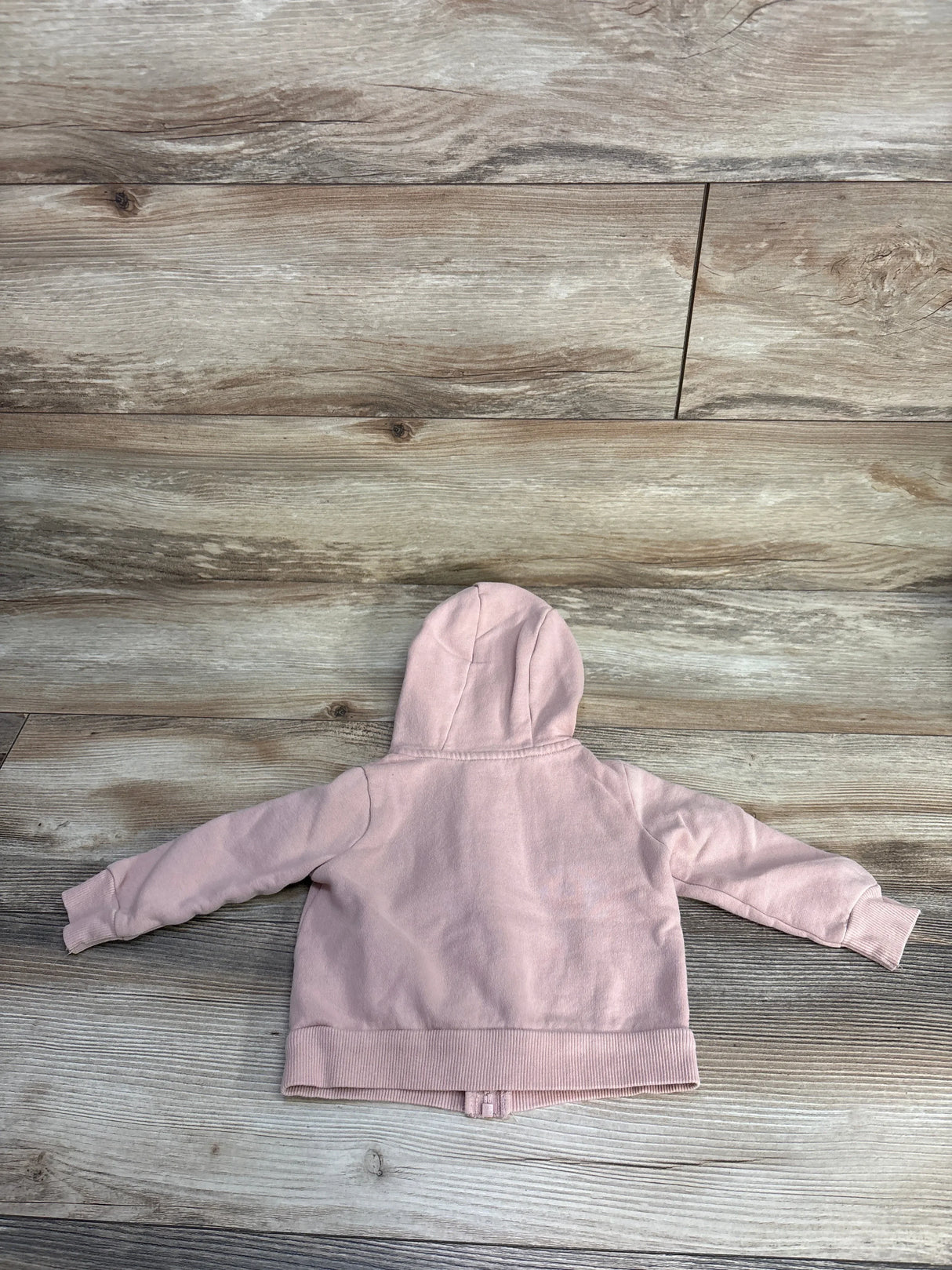 Back view of a pastel pink children's hoodie with long sleeves on a wooden floor