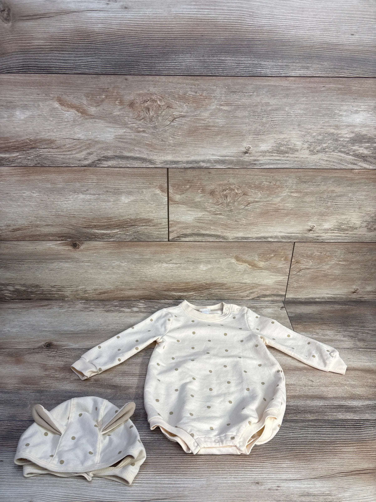 Flat lay of Cat & Jack polka dot sweatshirt bubble romper and hat set in ivory with wood plank background