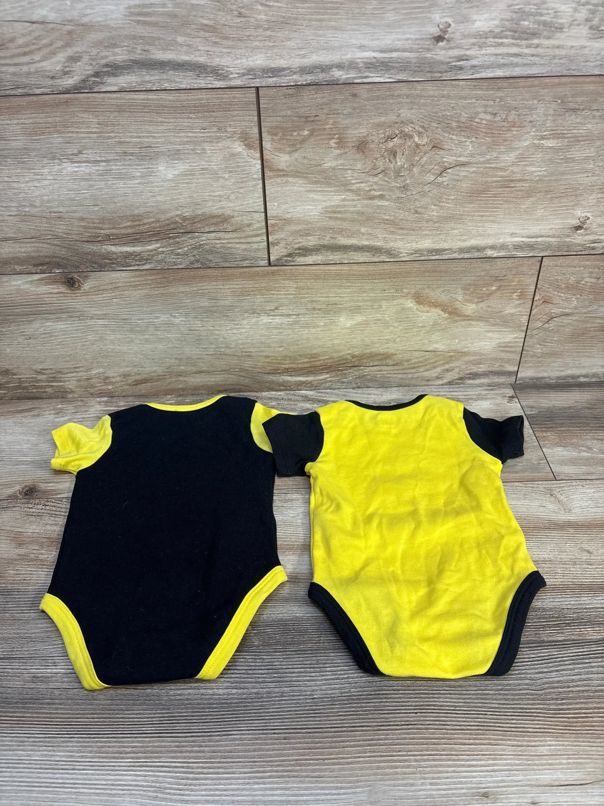 Two short-sleeve baby bodysuits in black and yellow on wood background