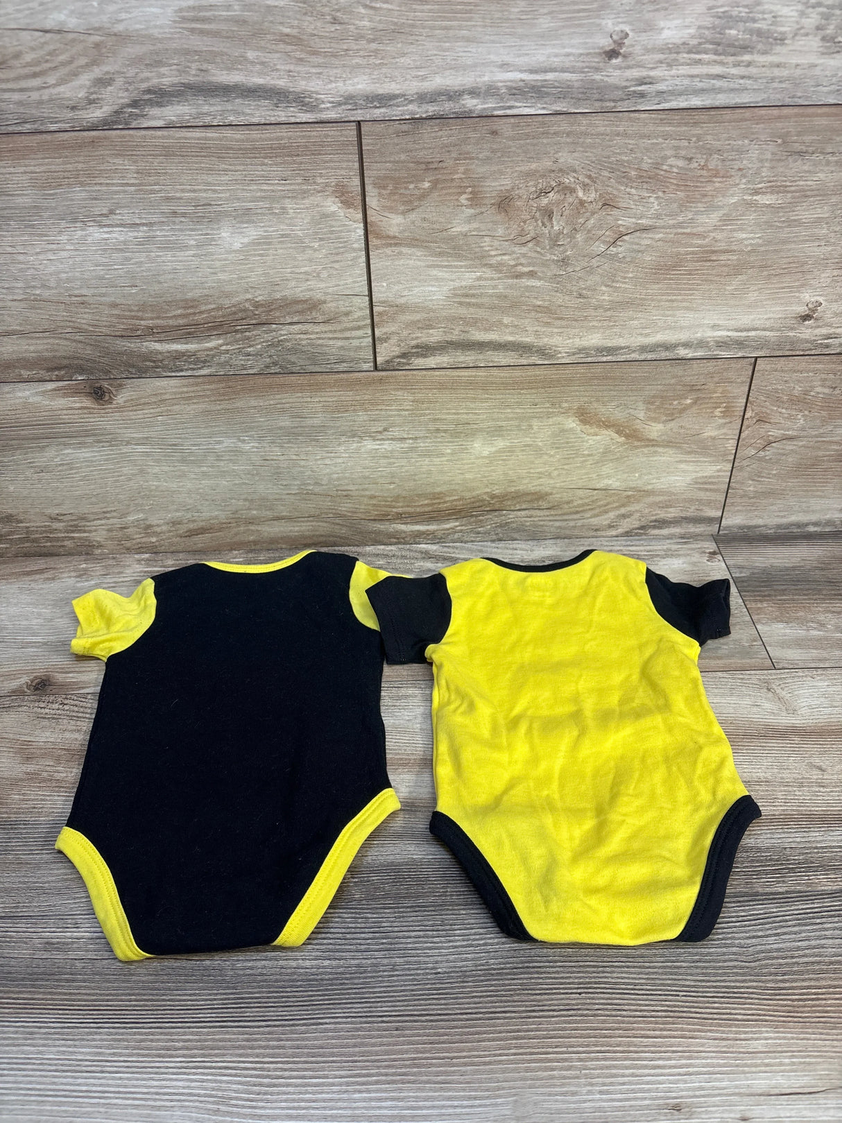 Two short-sleeve baby bodysuits in black and yellow on wood background