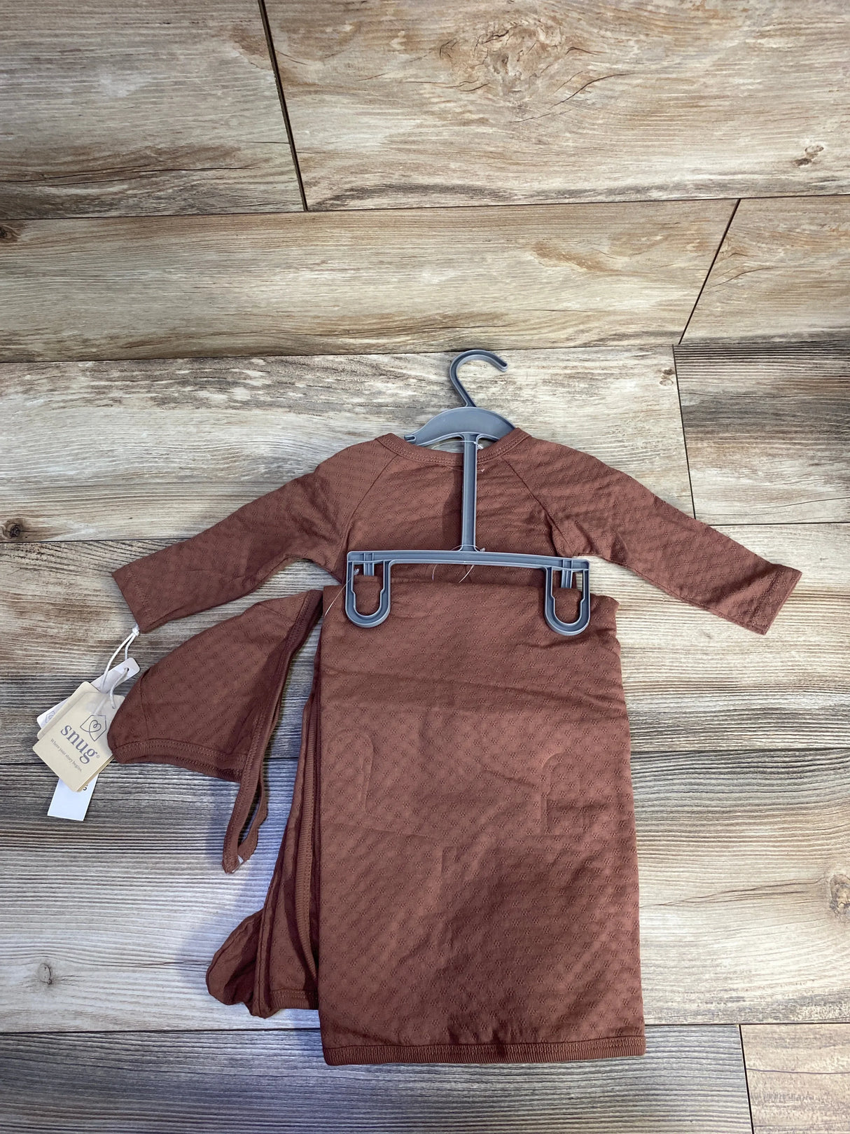 Brown long sleeve baby gown on hanger, snug brand, wood background