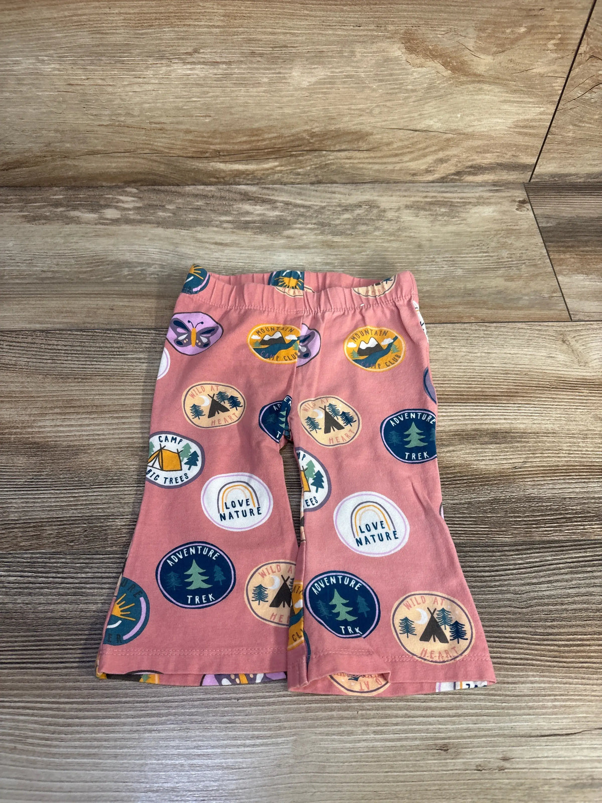 Flat lay of pink Cotton On Baby flared leggings showcasing colorful outdoor badge print on a wood-grain background