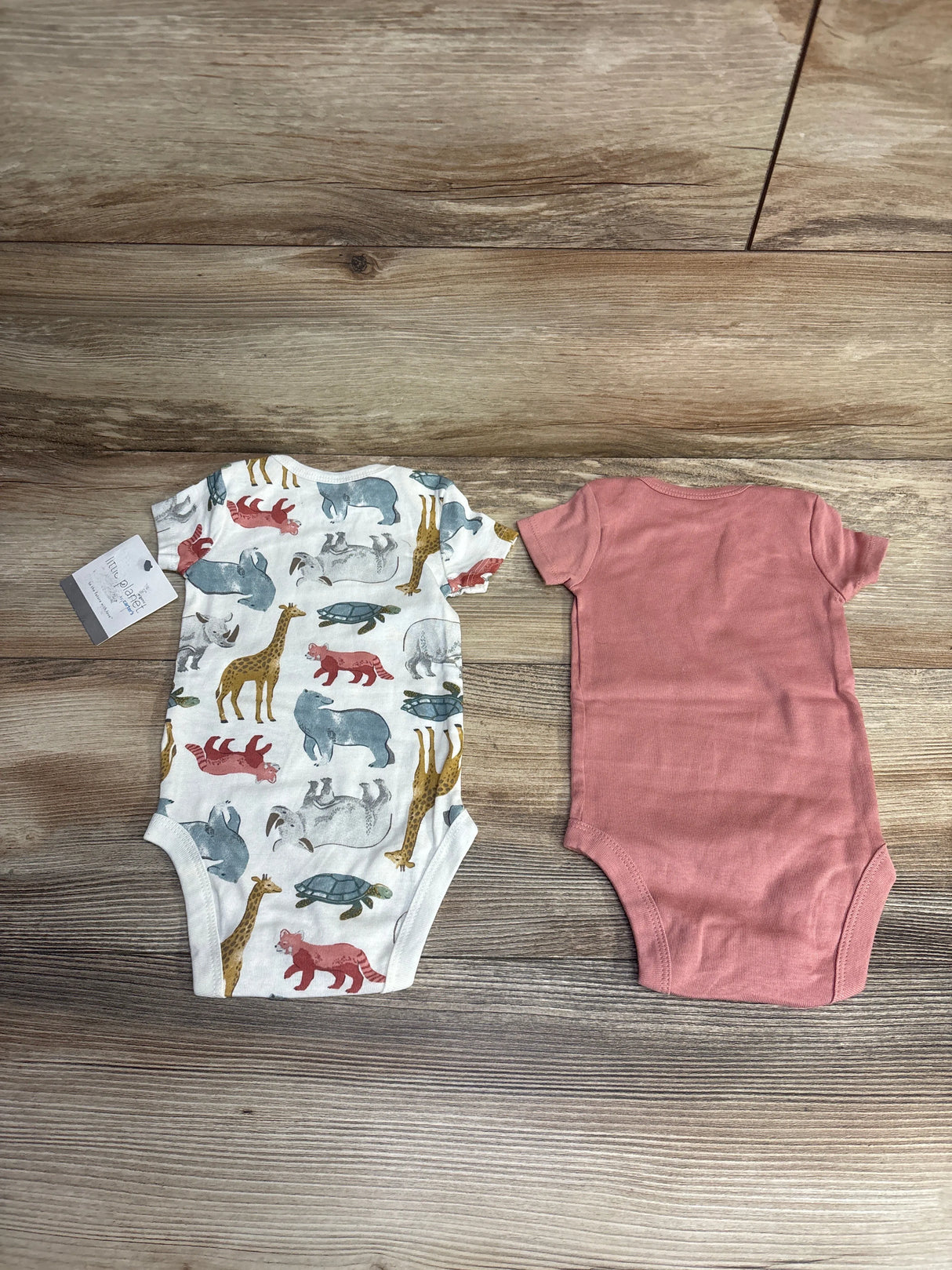 Two baby bodysuits laid flat on wood surface, one animal print and one solid dusty pink, kids clothes
