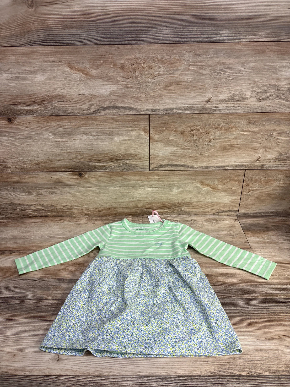 Baby dress with green striped long sleeves and a blue floral skirt on wooden floor