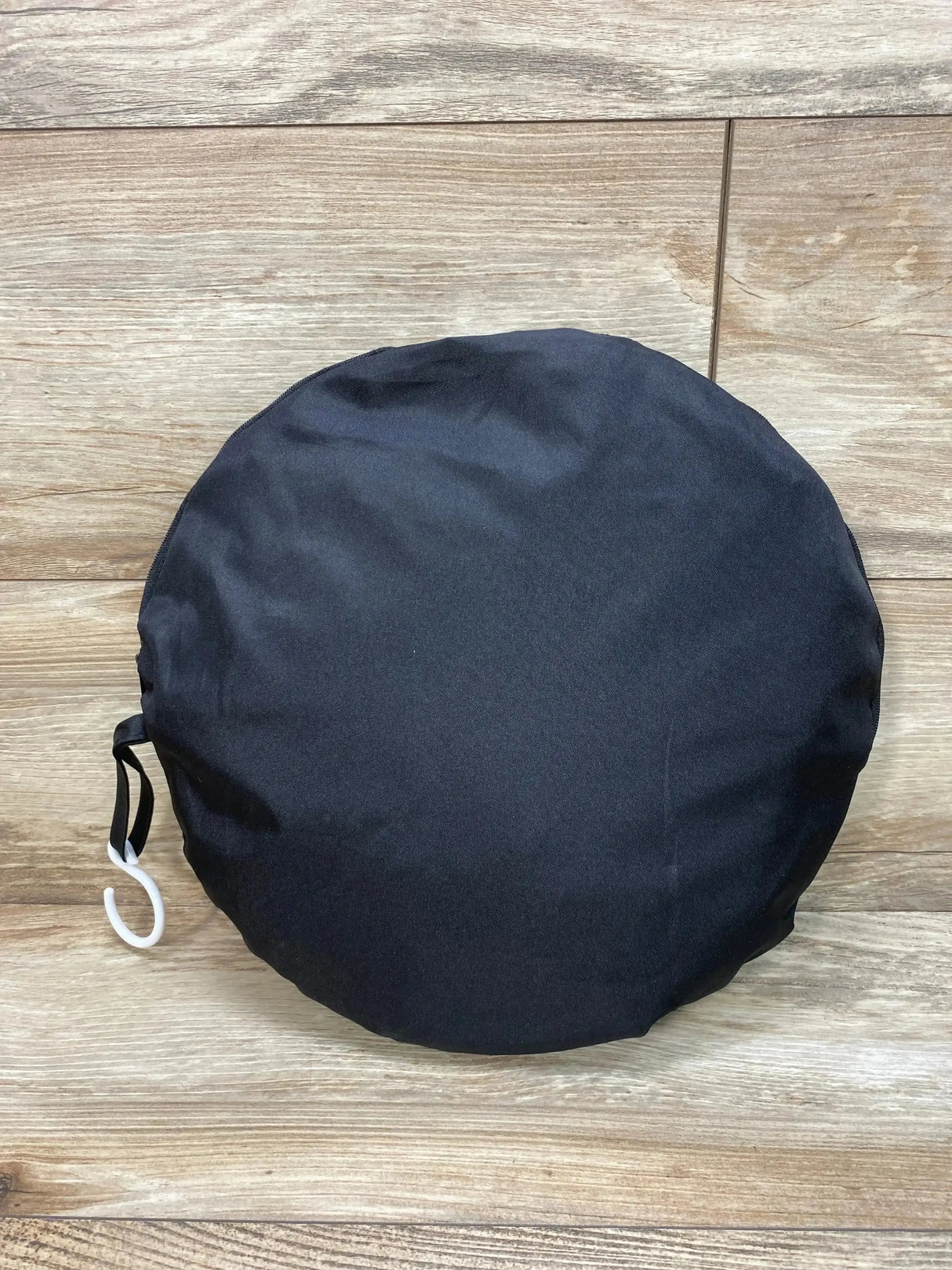 Top down view of Beberoad Love crib tent mosquito net folded in round black carrying pouch with white hook on wood floor